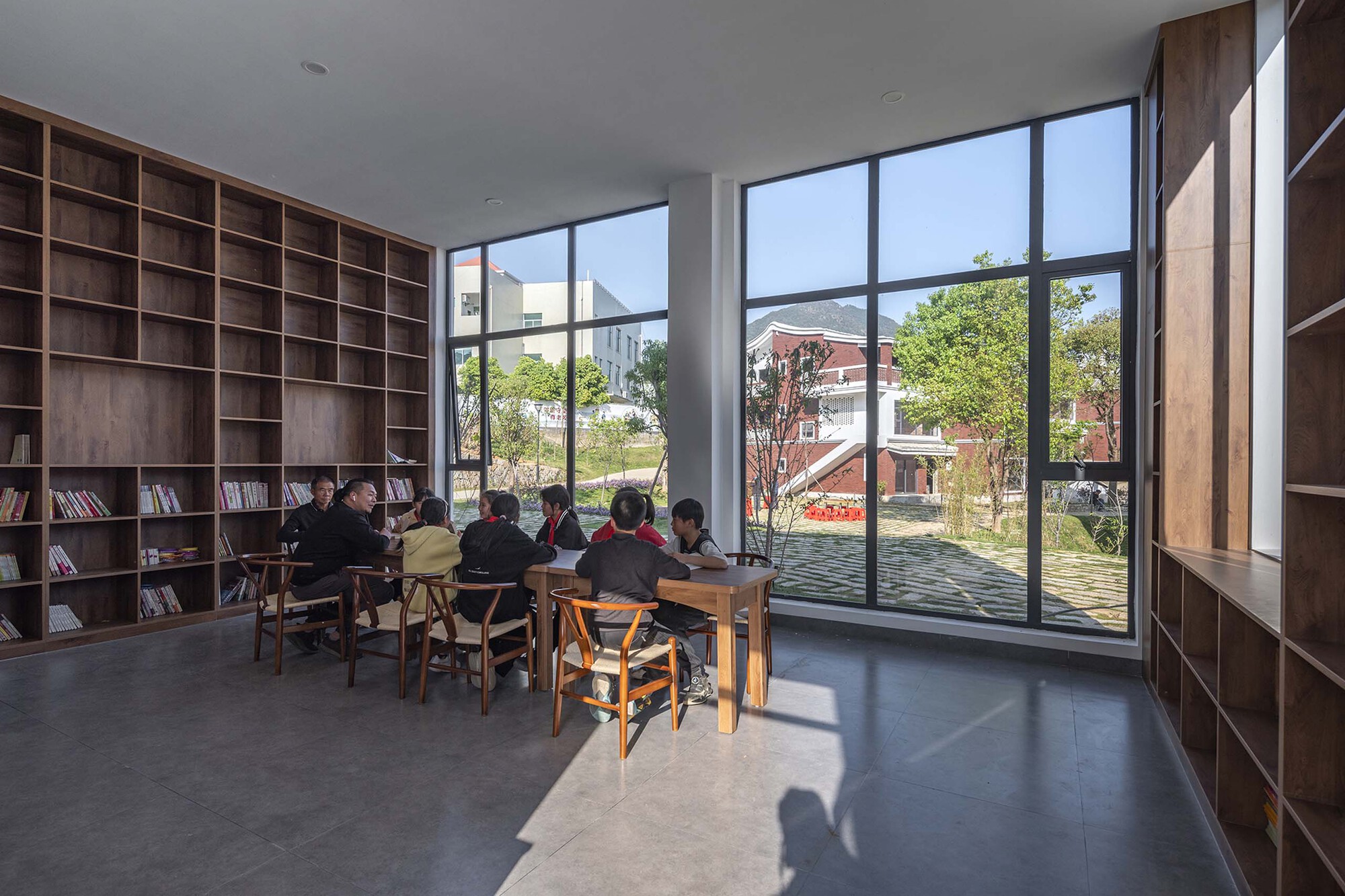 Library reading room with timber shelving and a group seated at tables by floor-to-ceiling windows