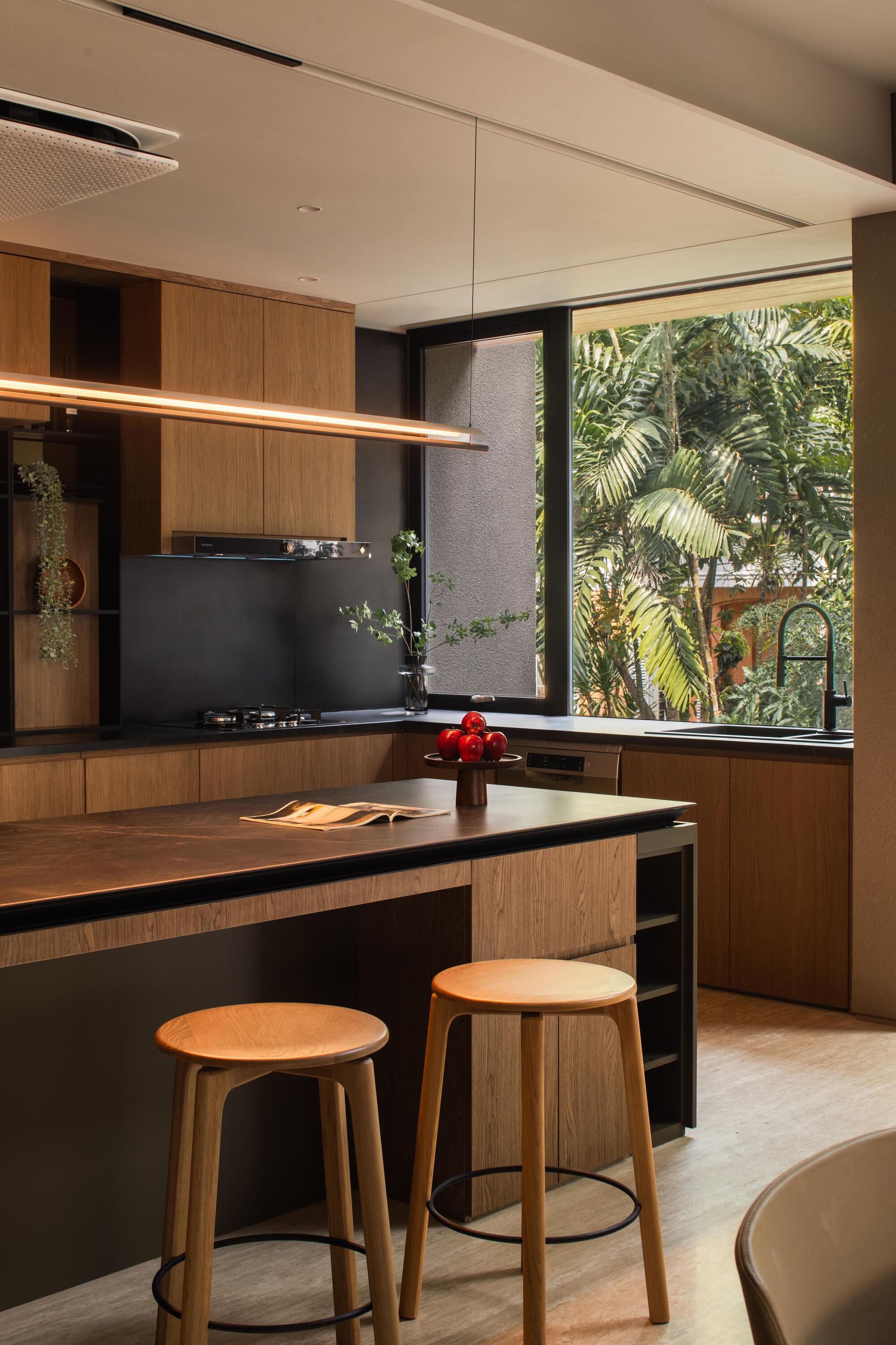 Kitchen island with timber cabinetry and corner window framing palm fronds in natural daylight