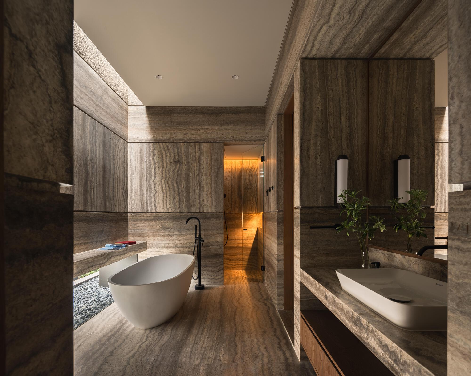 Bathroom with freestanding tub and striated stone wall cladding lit by concealed linear fixtures