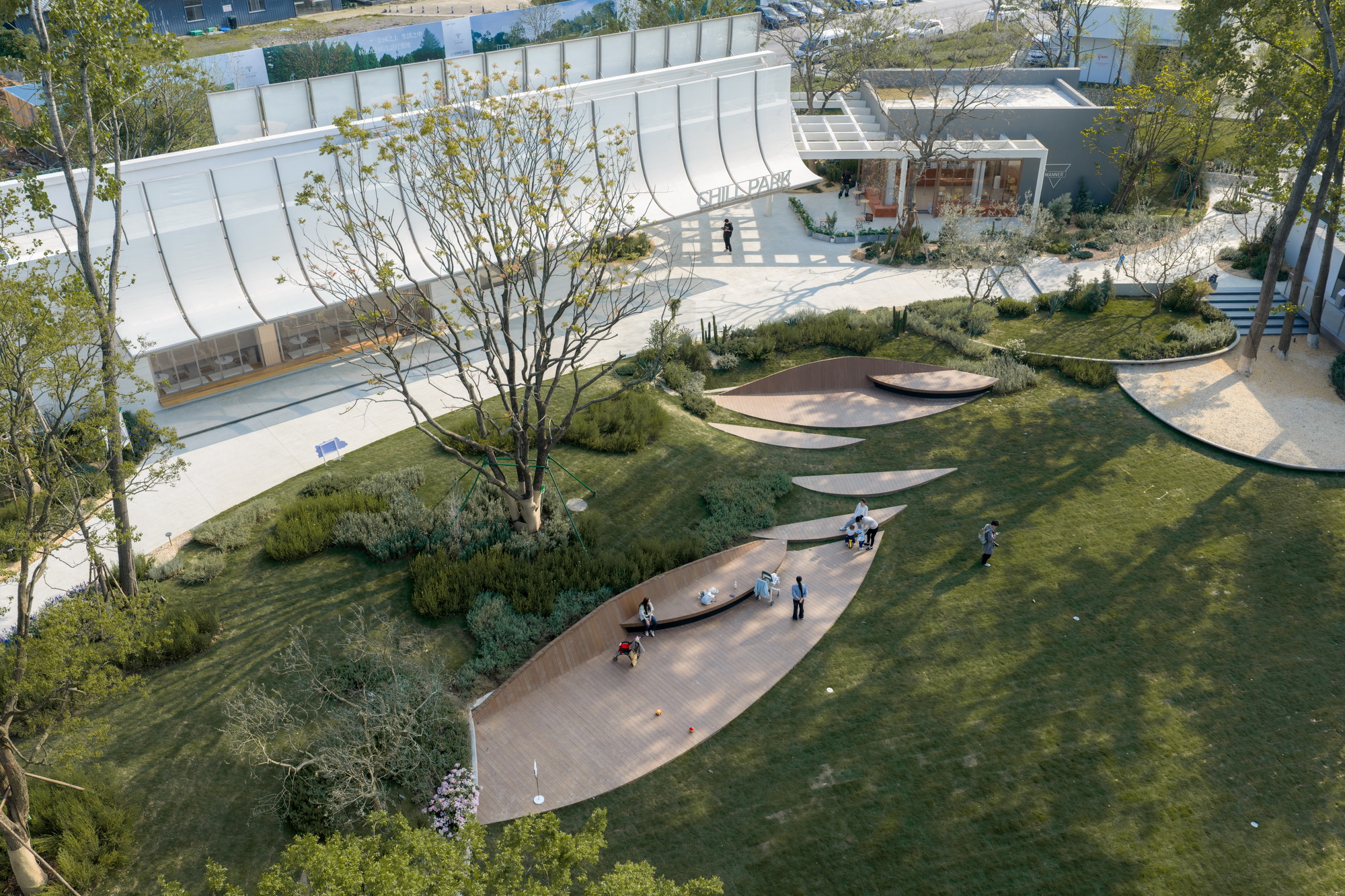 Aerial view of curving timber deck pathways threading through lawn and planted mounds with visitors
