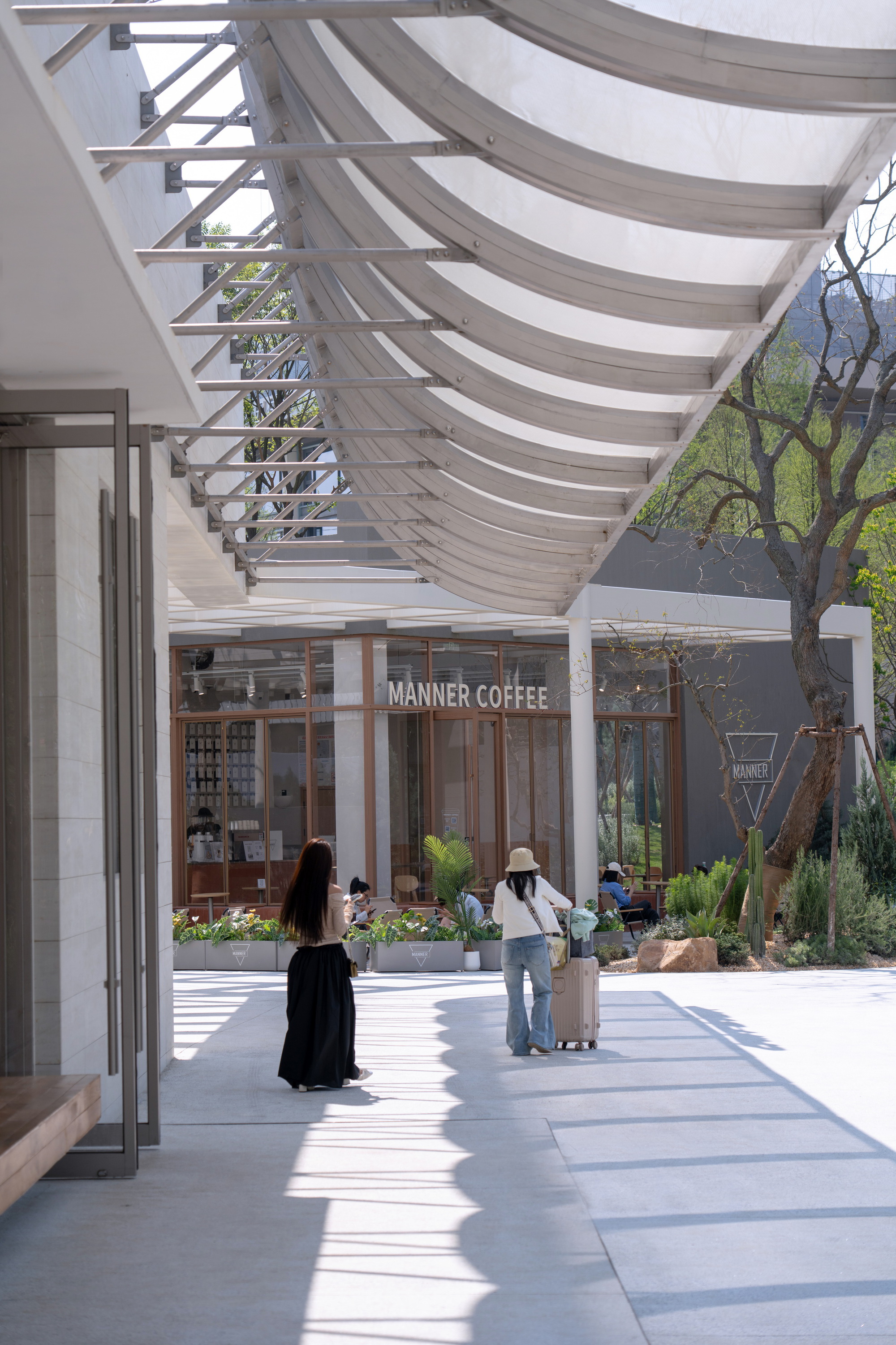 Covered walkway with undulating fabric canopy and steel framework casting shadows on pavement below