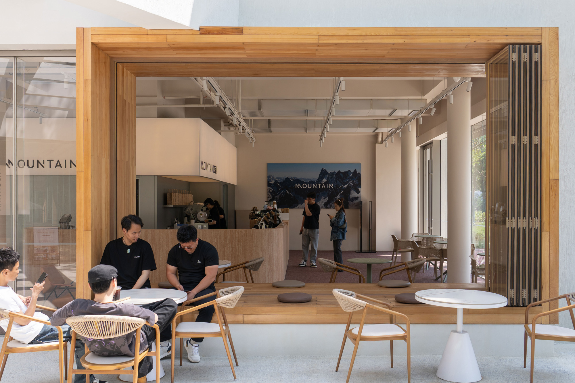 Timber-framed opening connecting interior cafe seating to outdoor tables with visitors gathered inside
