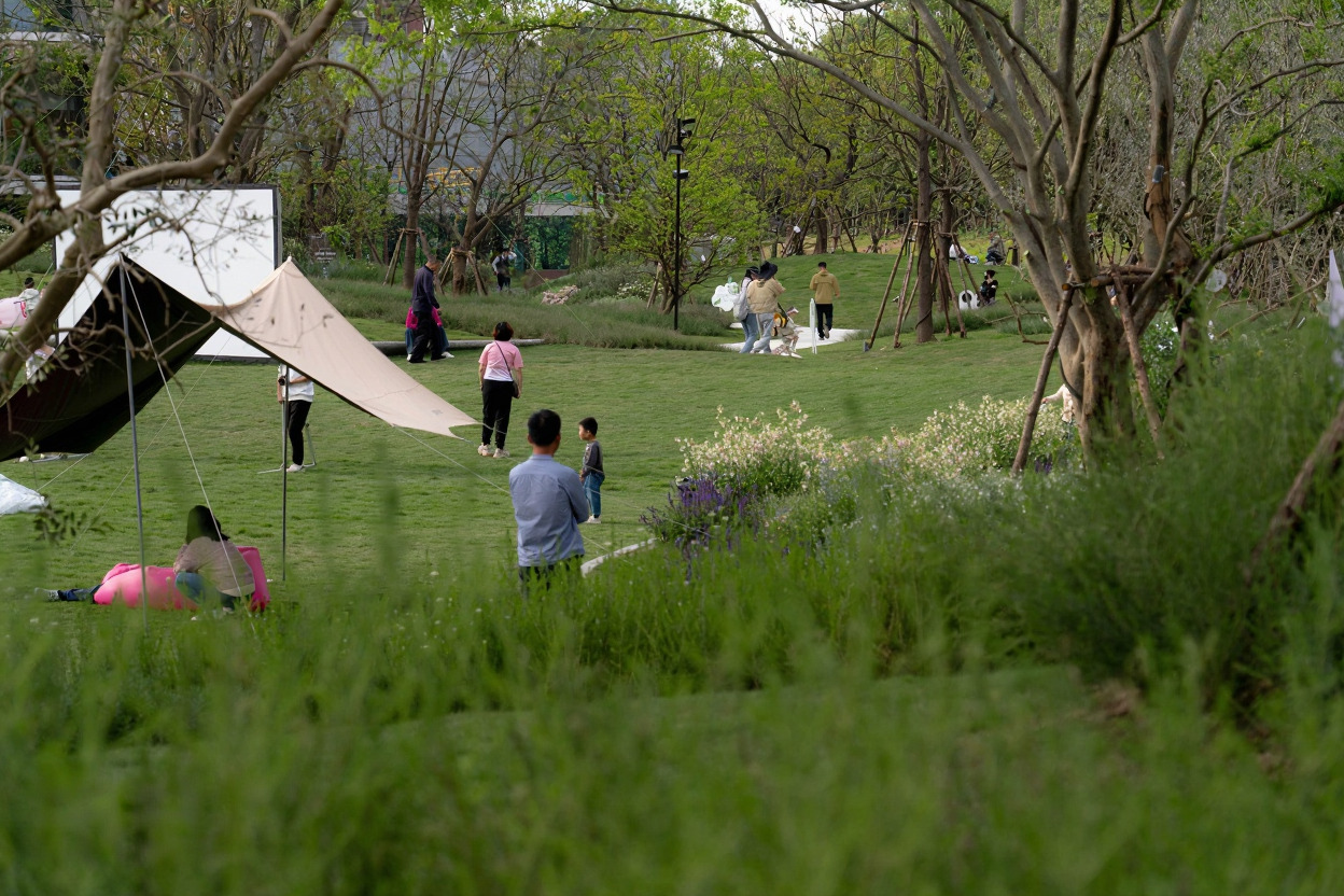 Park lawn with families beneath tent canopies among scattered trees and wildflower meadows