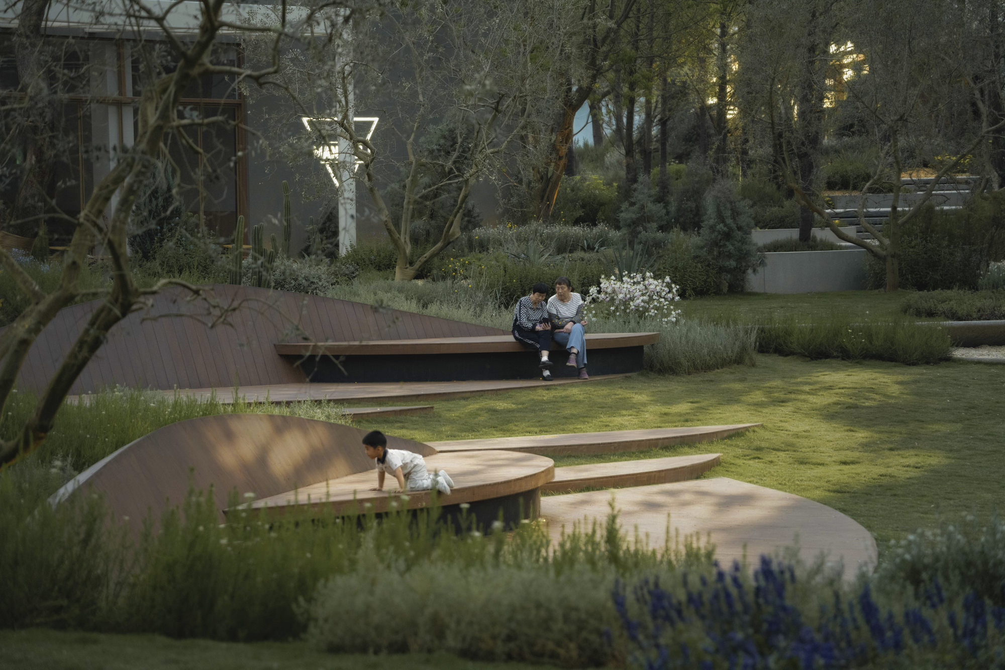 Circular timber seating platforms with children playing among planted beds and mature trees