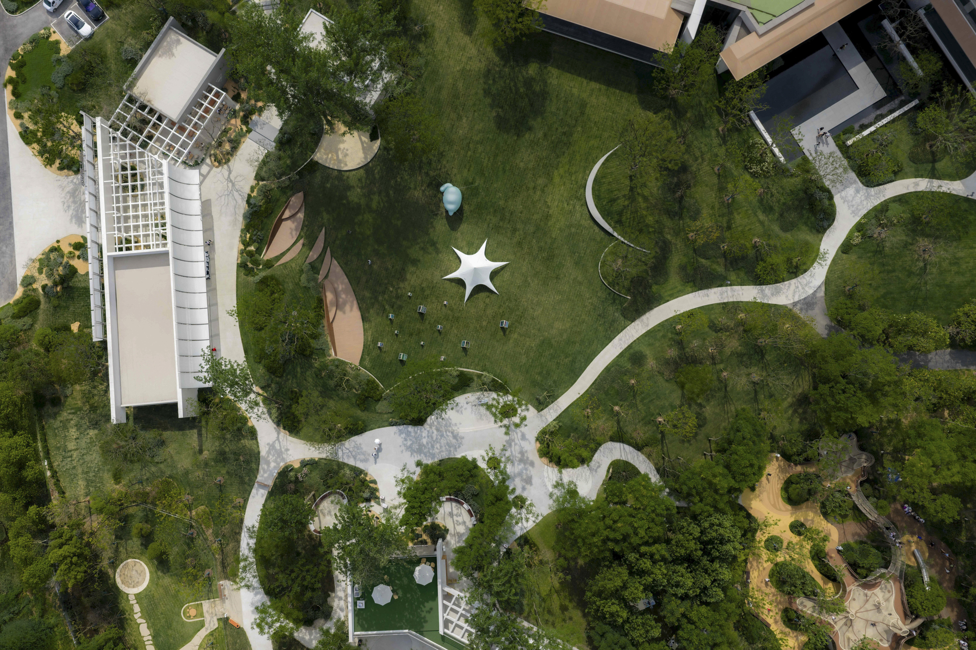 Overhead view of white star-shaped pavilion and meandering pathways through a green campus with trees