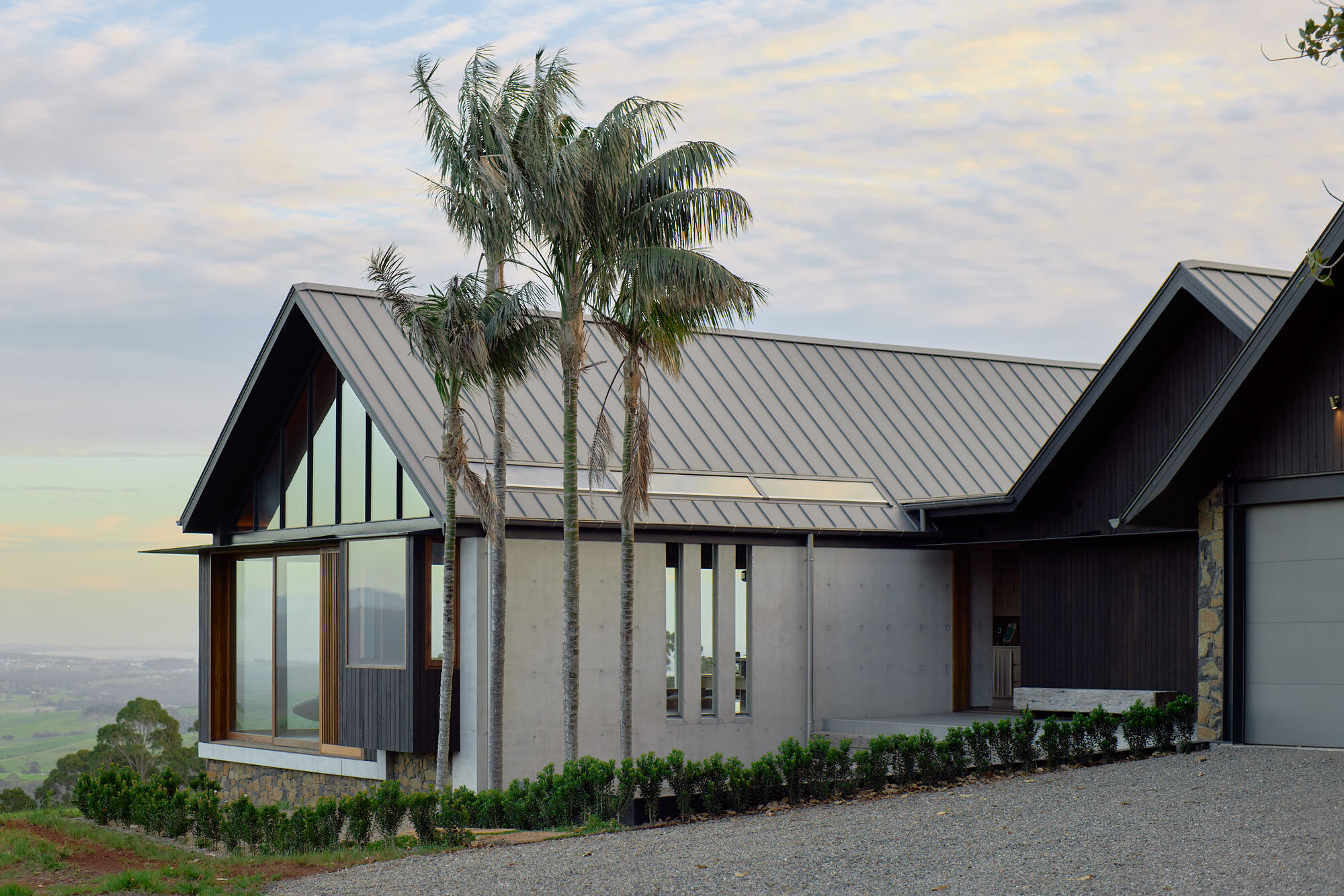 Entry facade with glazed gable and palm trees against a pale evening sky