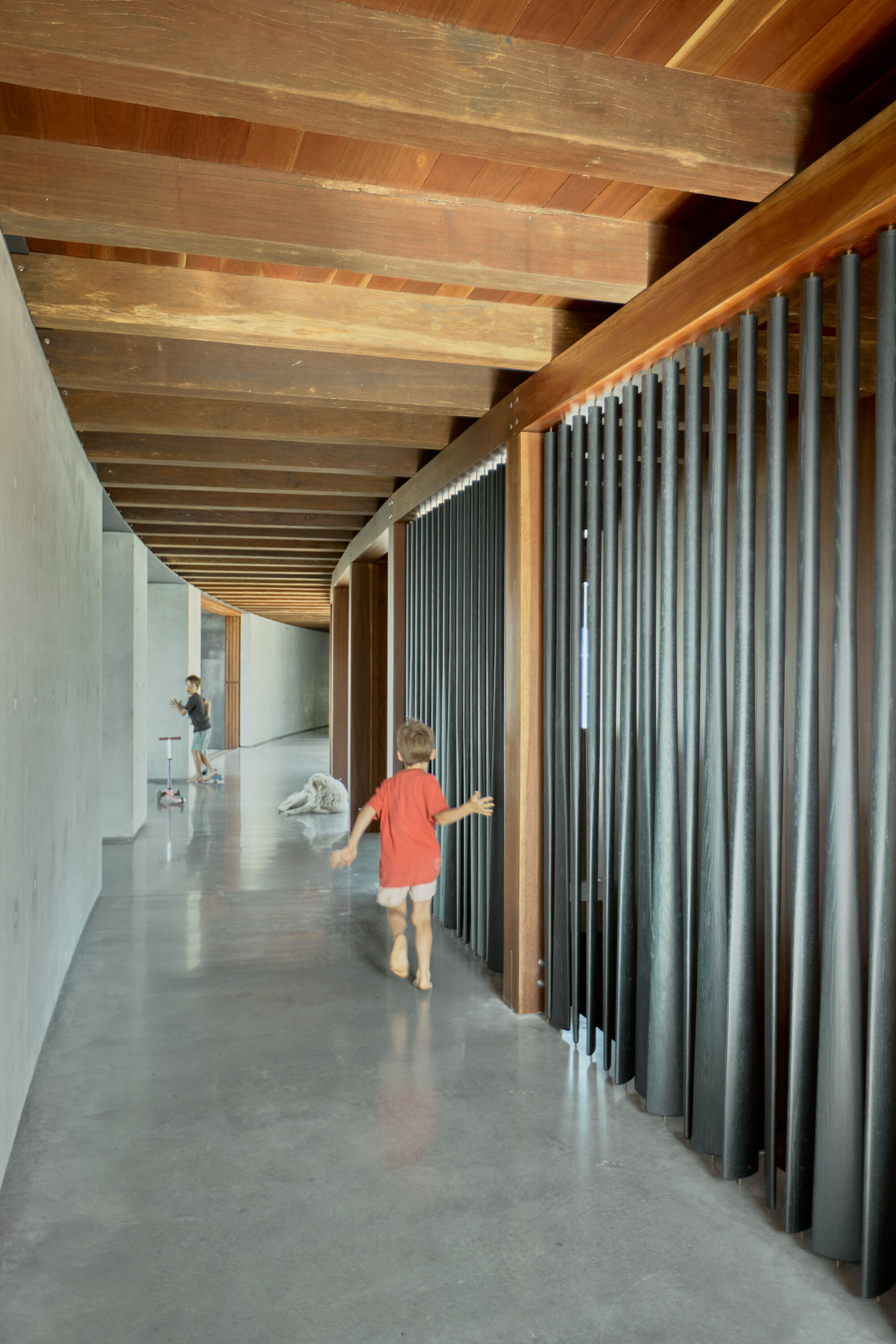 Corridor with corrugated metal screen and timber ceiling beams as a child walks along polished concrete