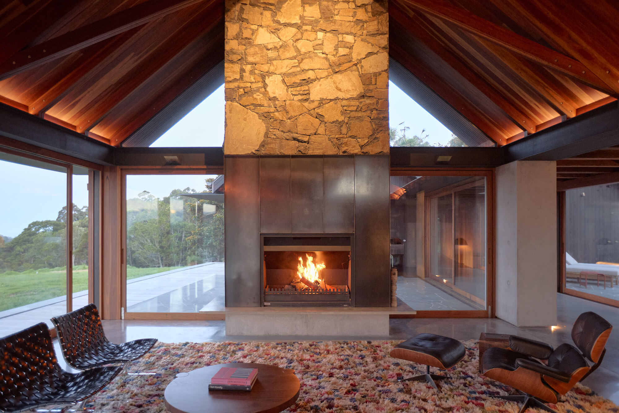 Stone chimney with steel fireplace surround beneath a pitched timber ceiling at twilight