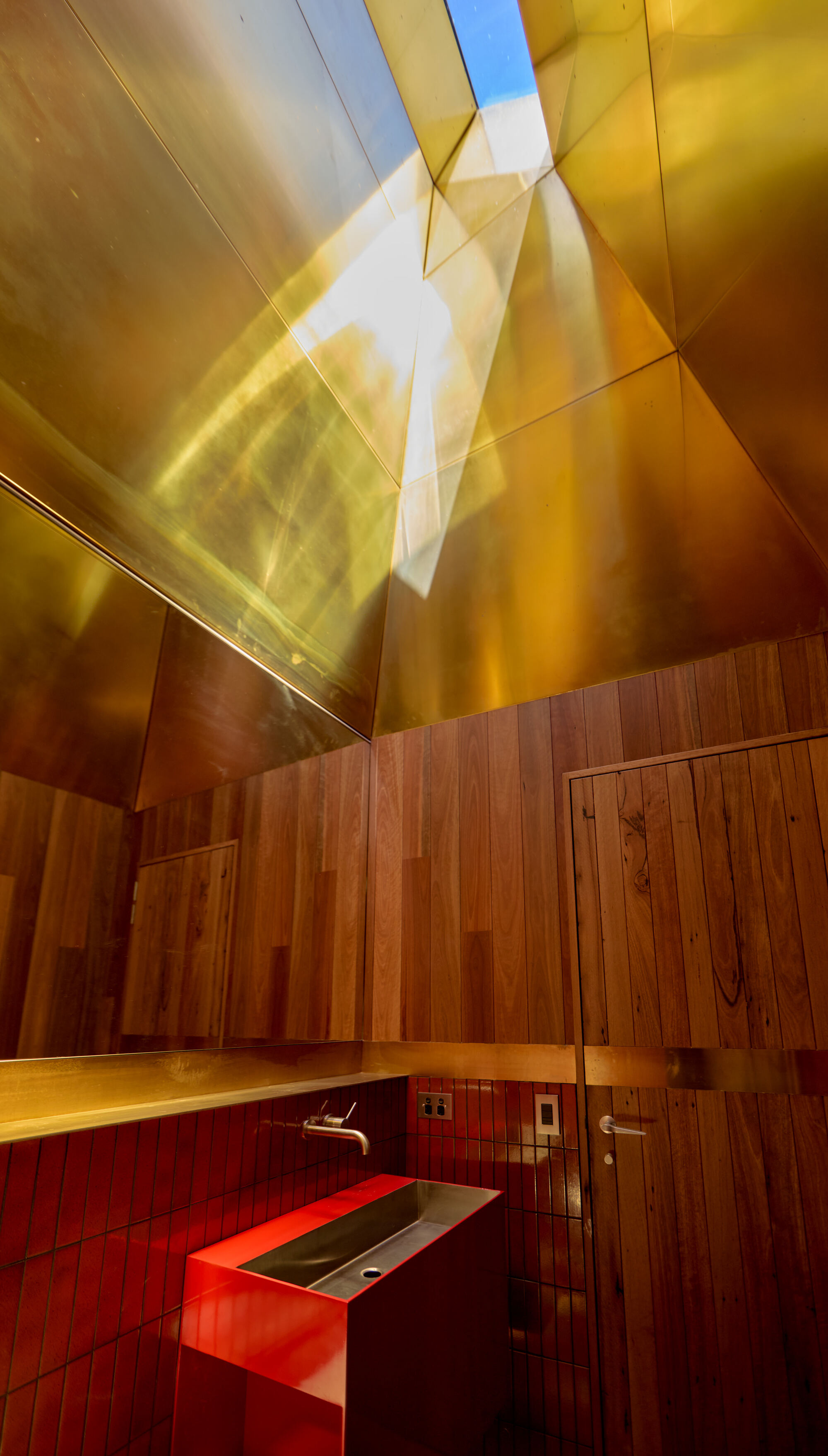 Bathroom with red steel sink and timber walls beneath a gold metal ceiling skylight