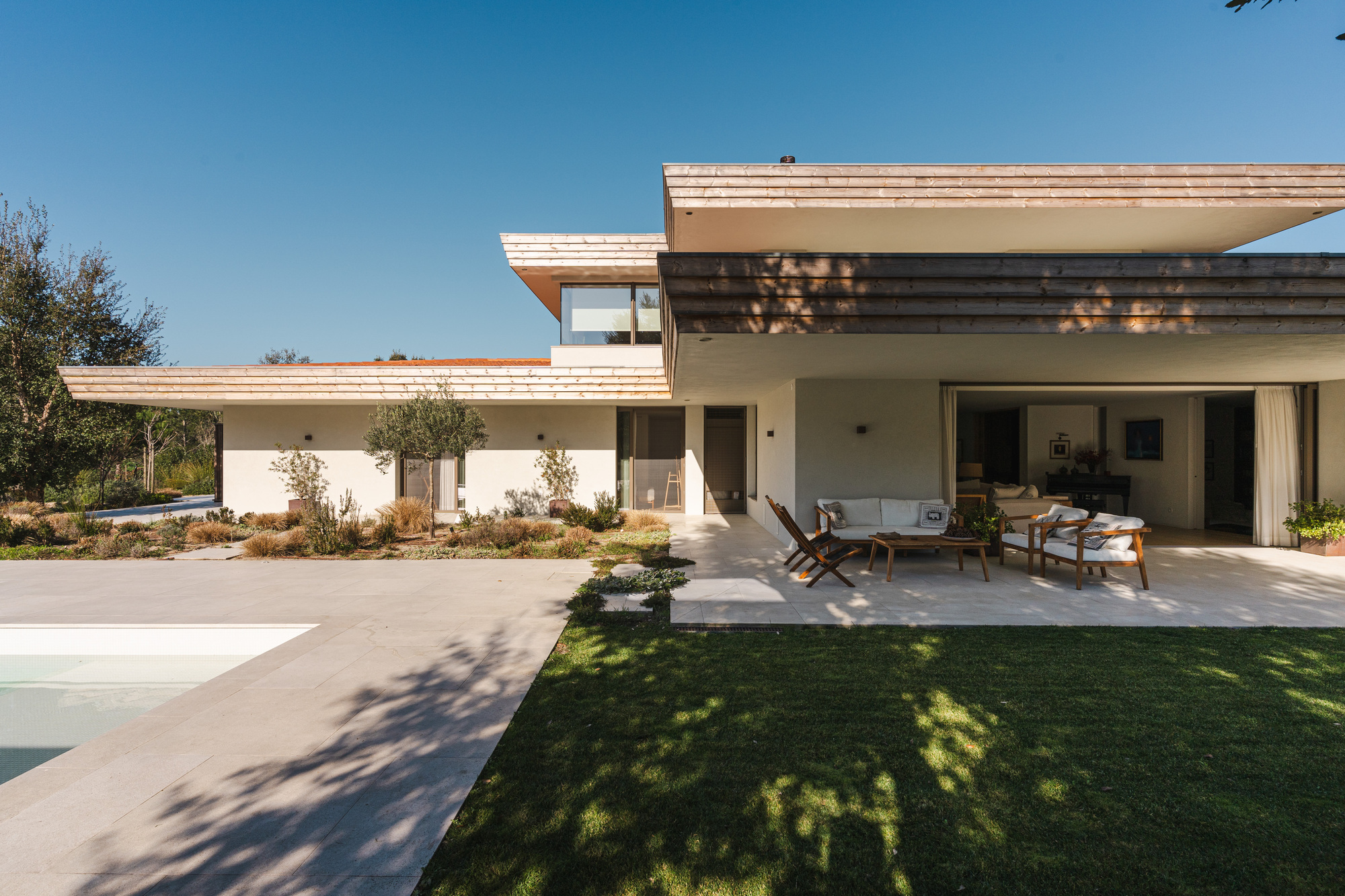 Covered terrace with timber ceiling overhang and furnished outdoor seating overlooking a lawn and trees