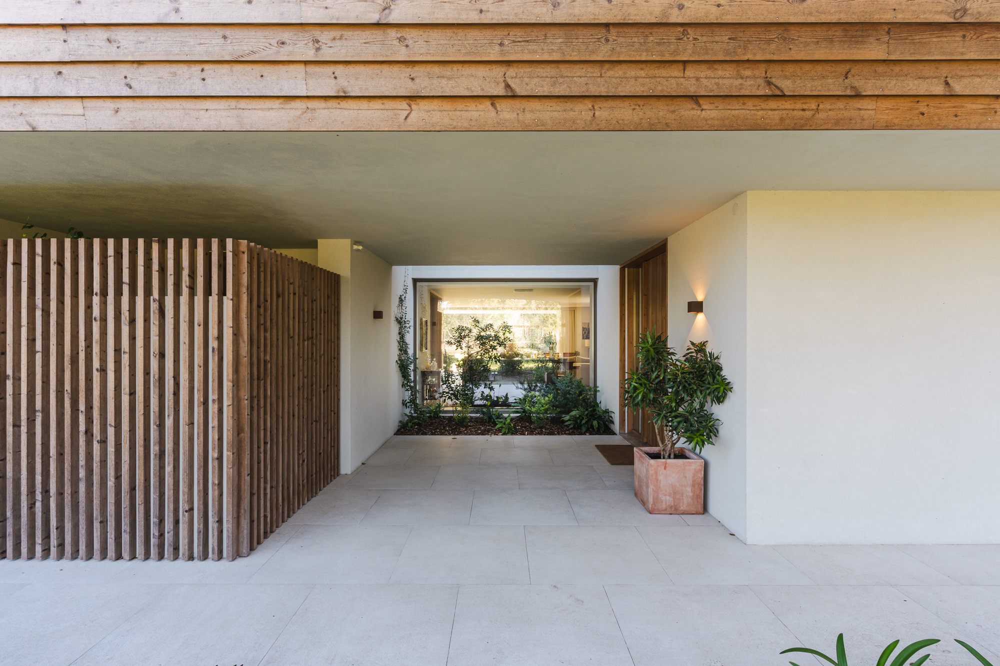 Covered entry passage with timber slat wall and exposed wood ceiling framing an interior courtyard view