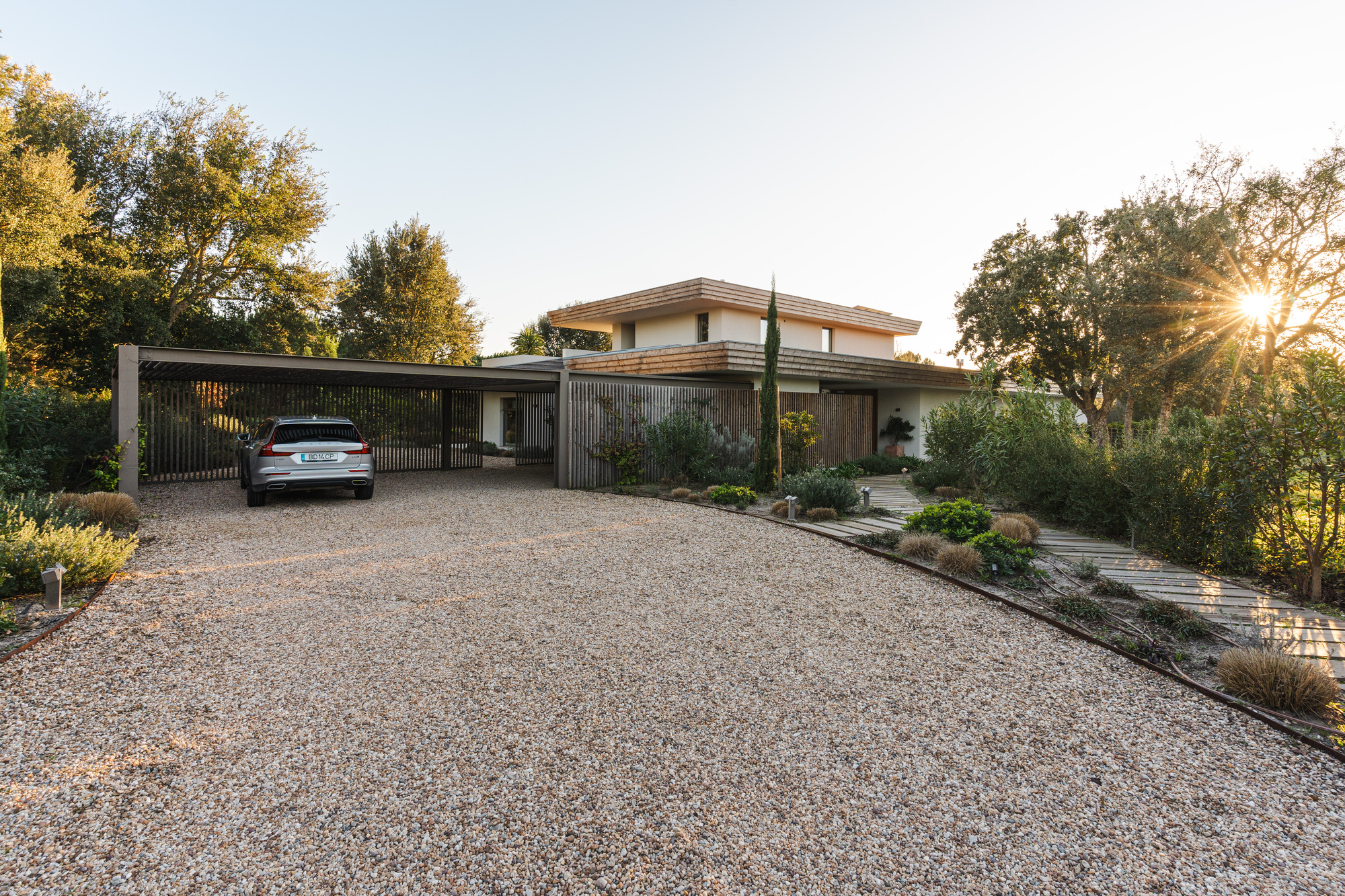 Gravel driveway with carport and timber slat screens beneath a tile roof at sunset