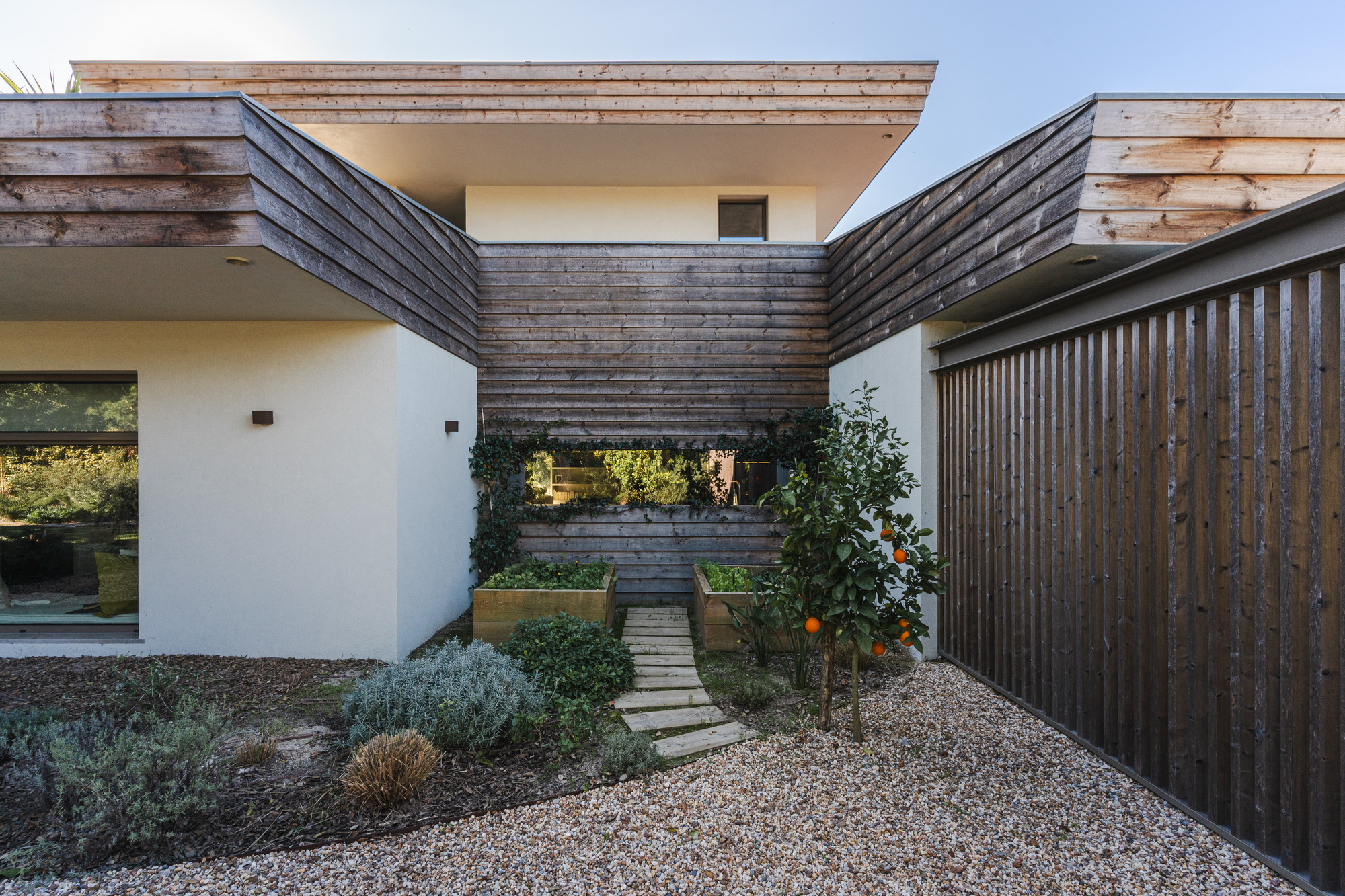 Courtyard entry with weathered timber cladding and gravel path leading between planted beds at dusk