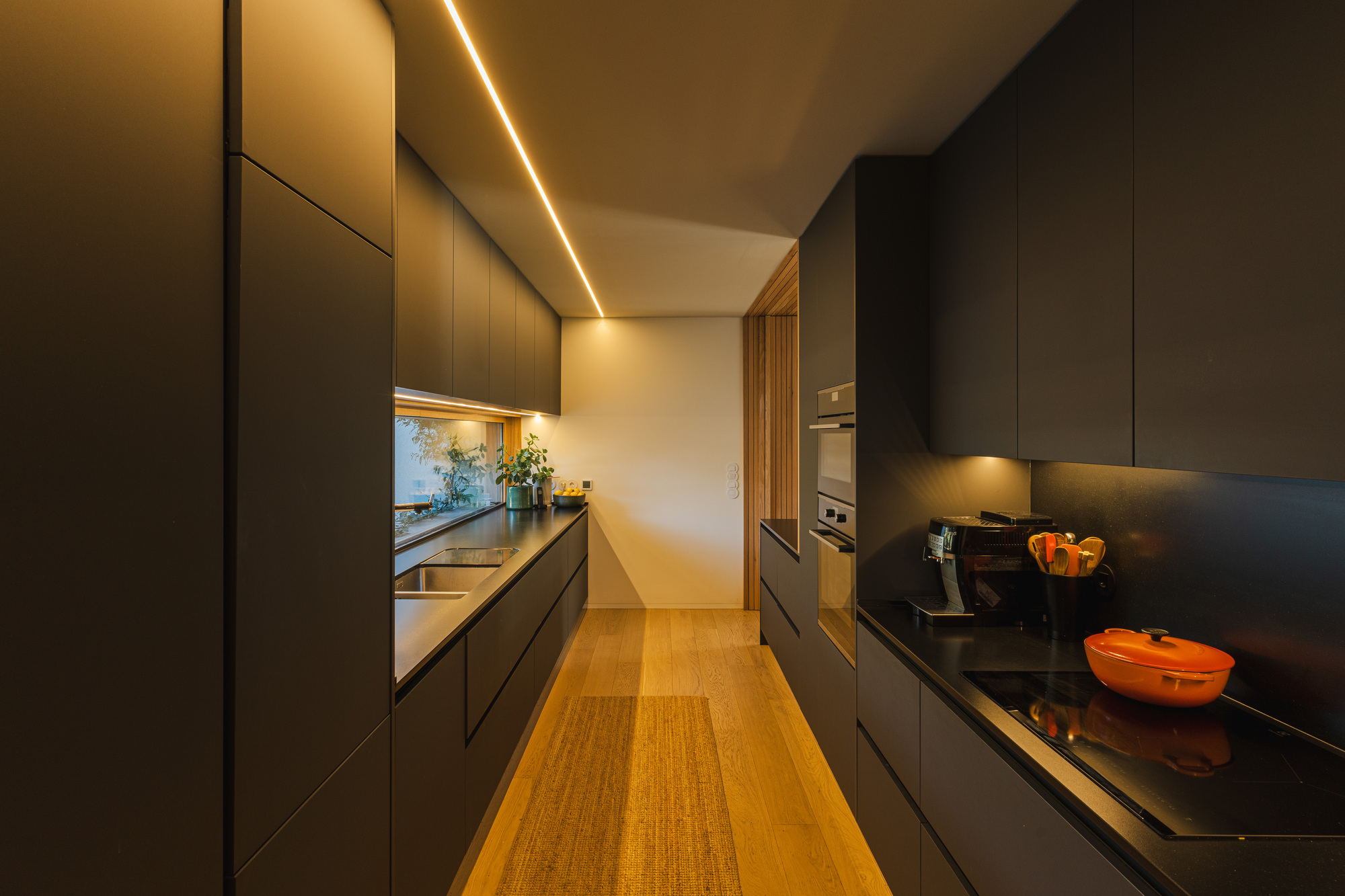 Galley kitchen with dark grey cabinetry, recessed LED strip lighting and light timber flooring