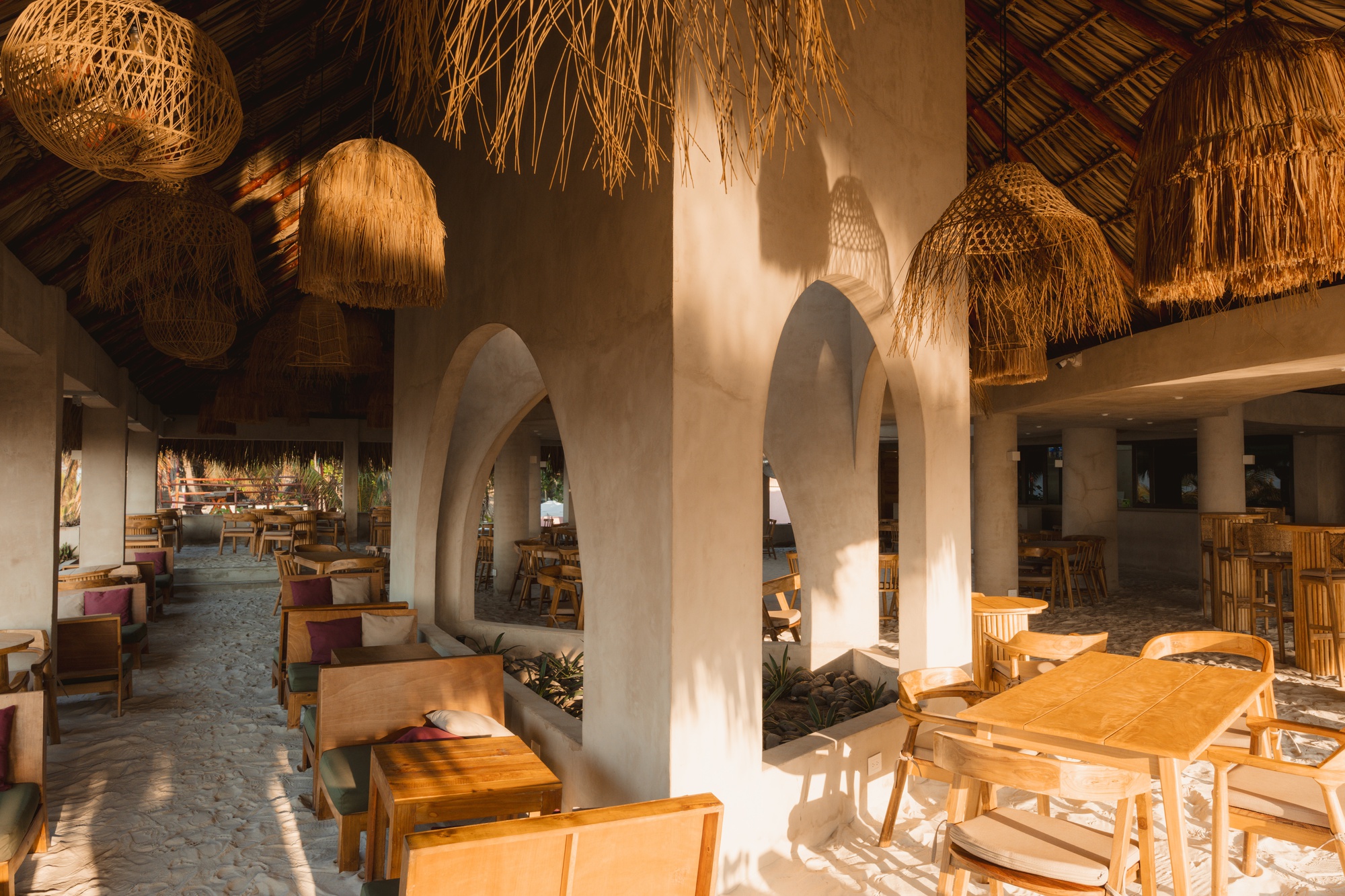 View through the arched interior colonnade with thatched roof and sunlight streaming across the polished floor