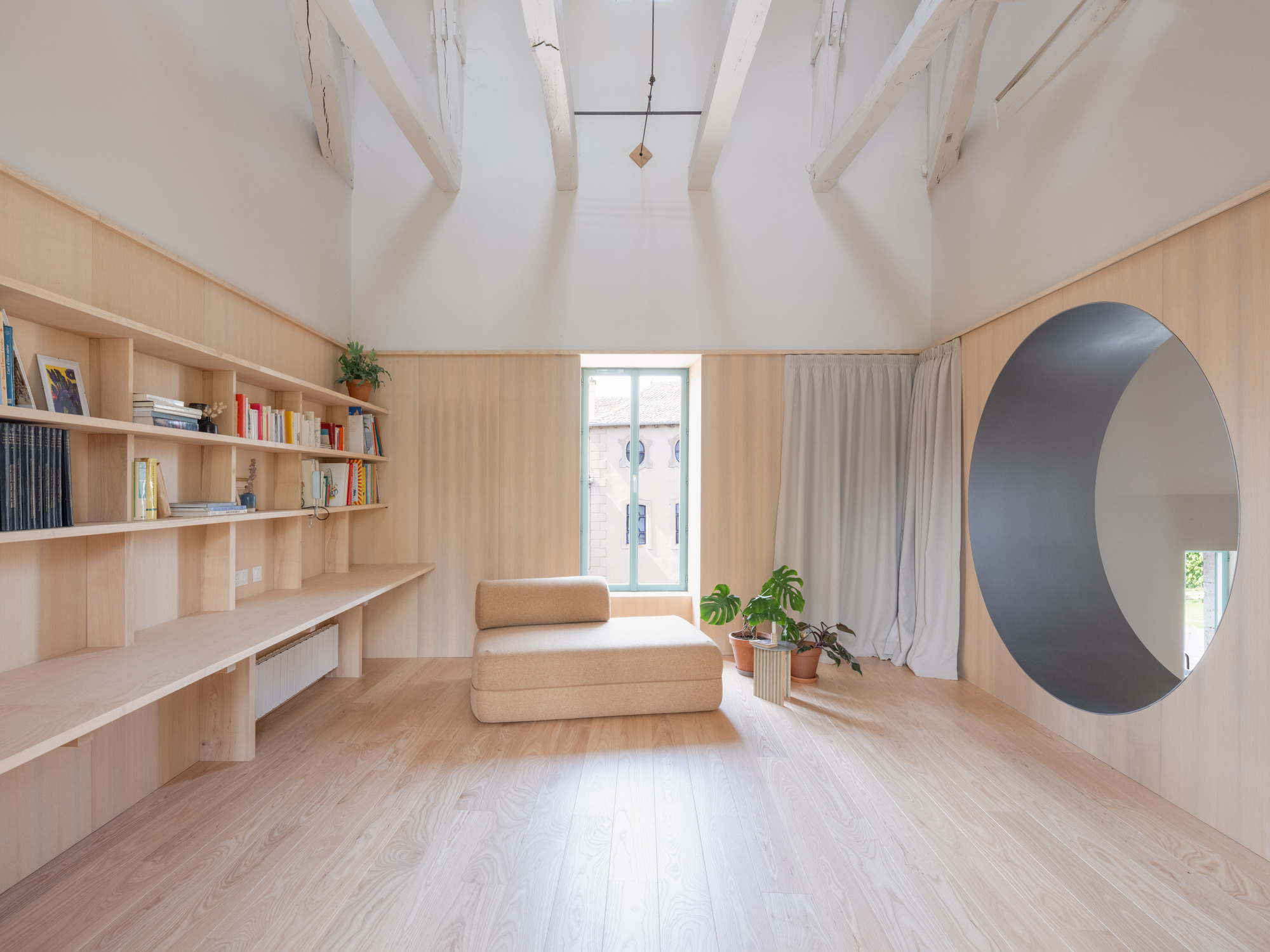 Interior room with exposed timber rafters, plywood built-in shelving and circular portal opening in soft daylight