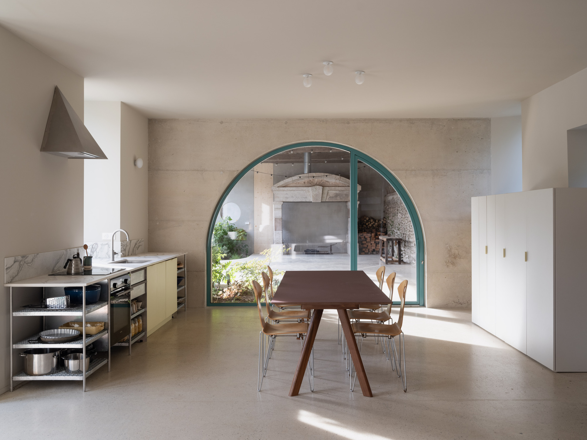 Open kitchen and dining area viewed through large arched doorway with teal frame and stone wall beyond