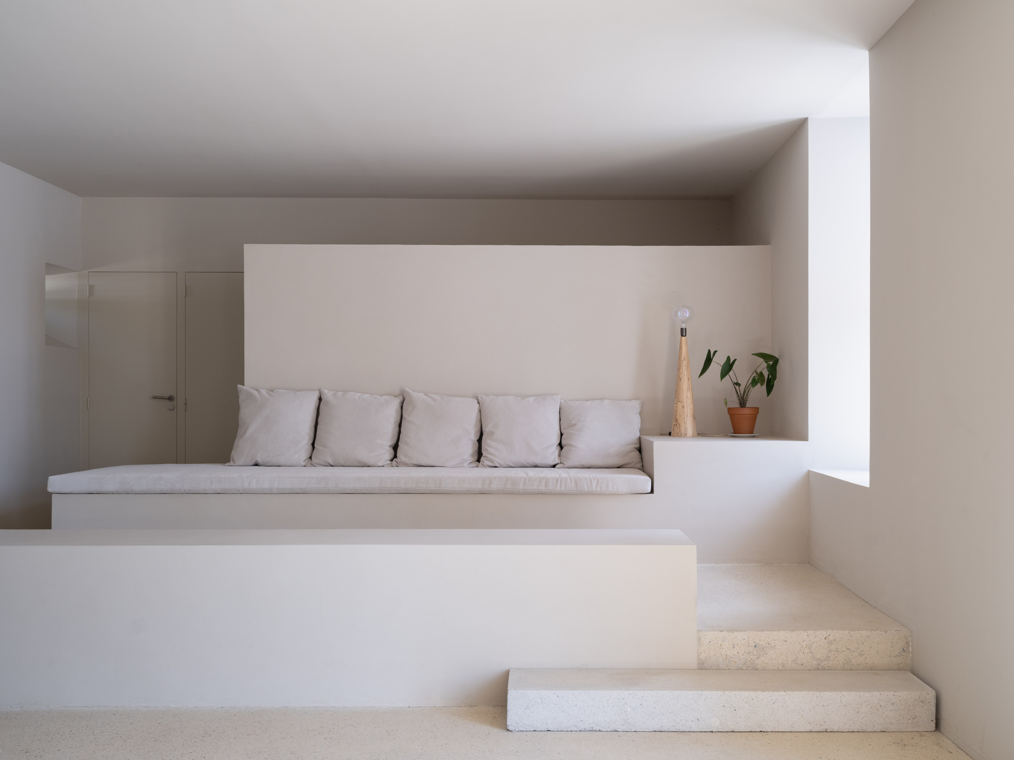 Built-in seating nook with white cushions and stone steps ascending under a low ceiling