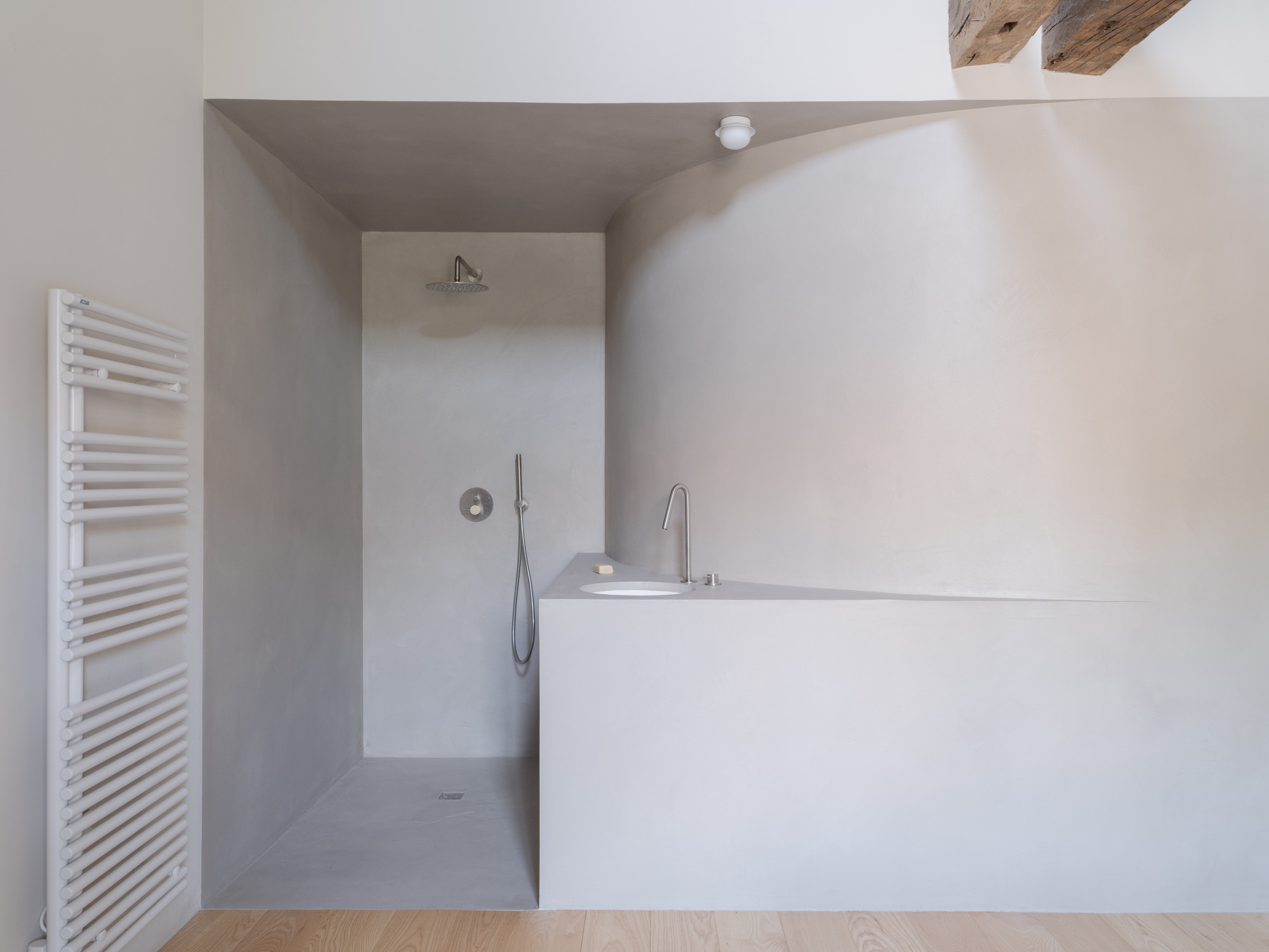 Bathroom with tadelakt-finished bathtub and walk-in shower alcove under exposed timber beams