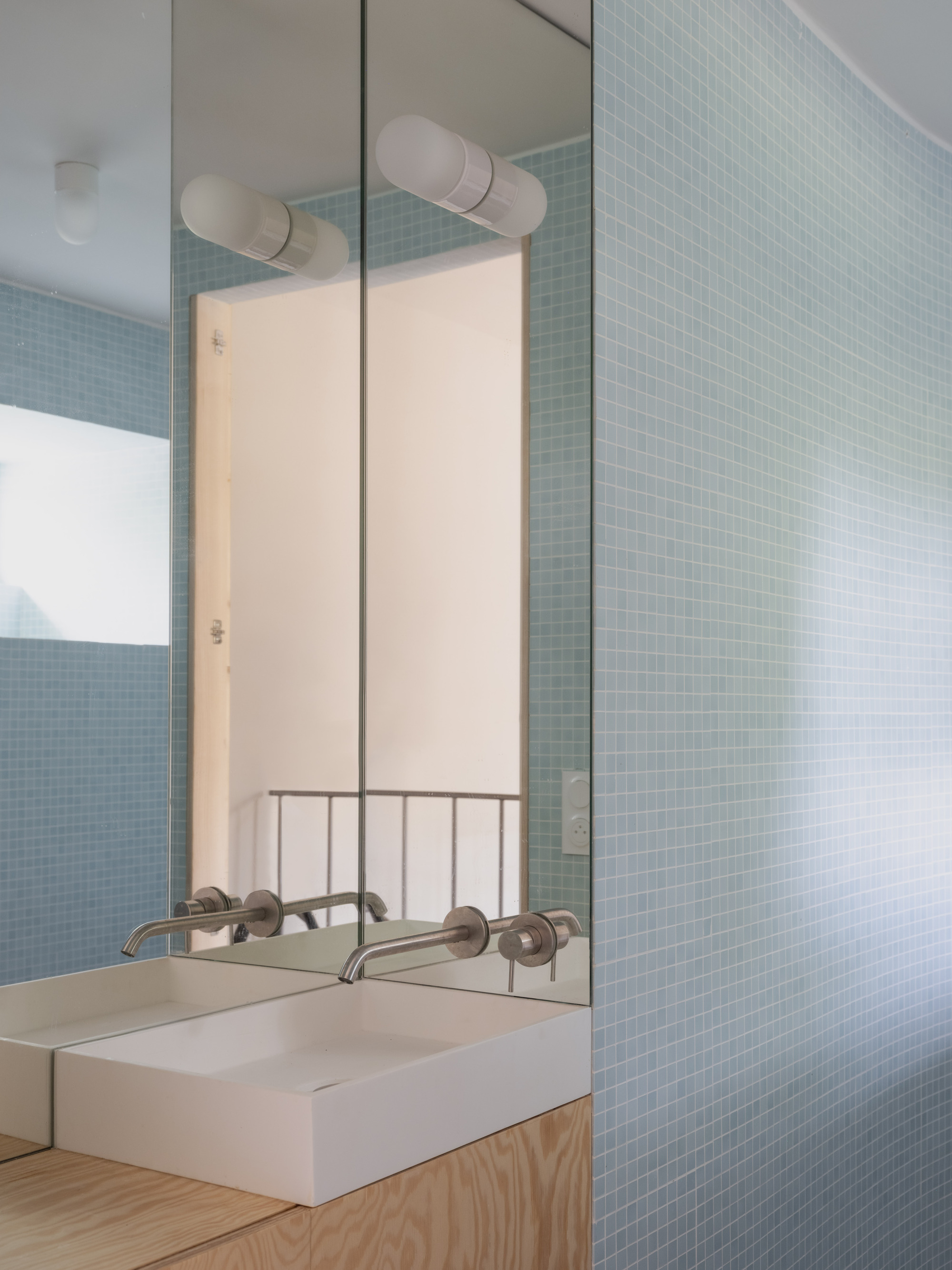 Bathroom mirror reflecting pale blue mosaic tile wall and handrail with timber vanity below