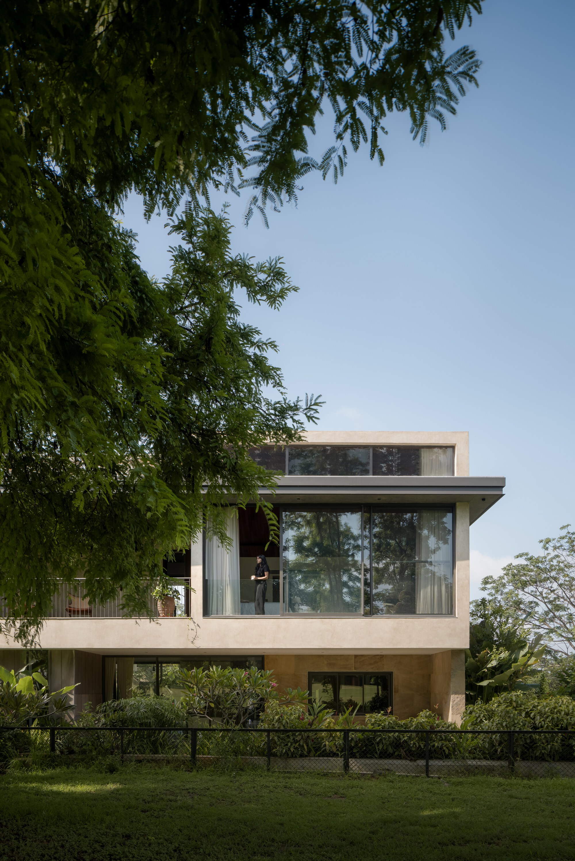 Three-story facade with stacked terraces and glazing framed by overhanging tree branches