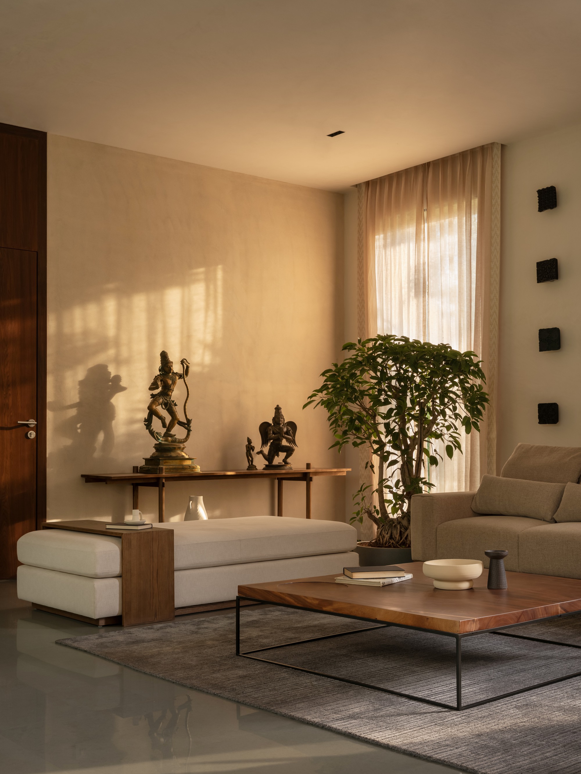 Living room with sheer curtains filtering afternoon light onto a wall displaying sculpture on a console