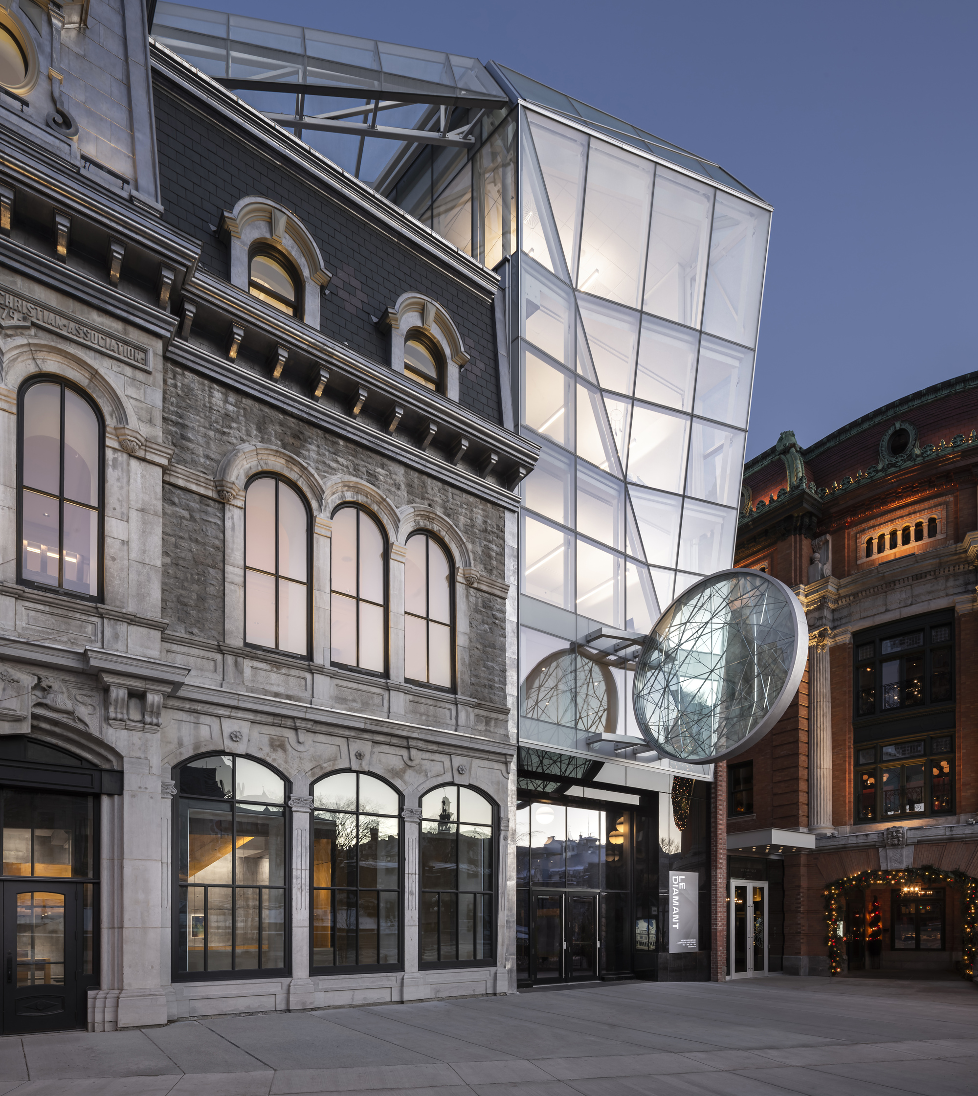 Entrance facade with arched openings and illuminated glass tower rising above the mansard roof at twilight