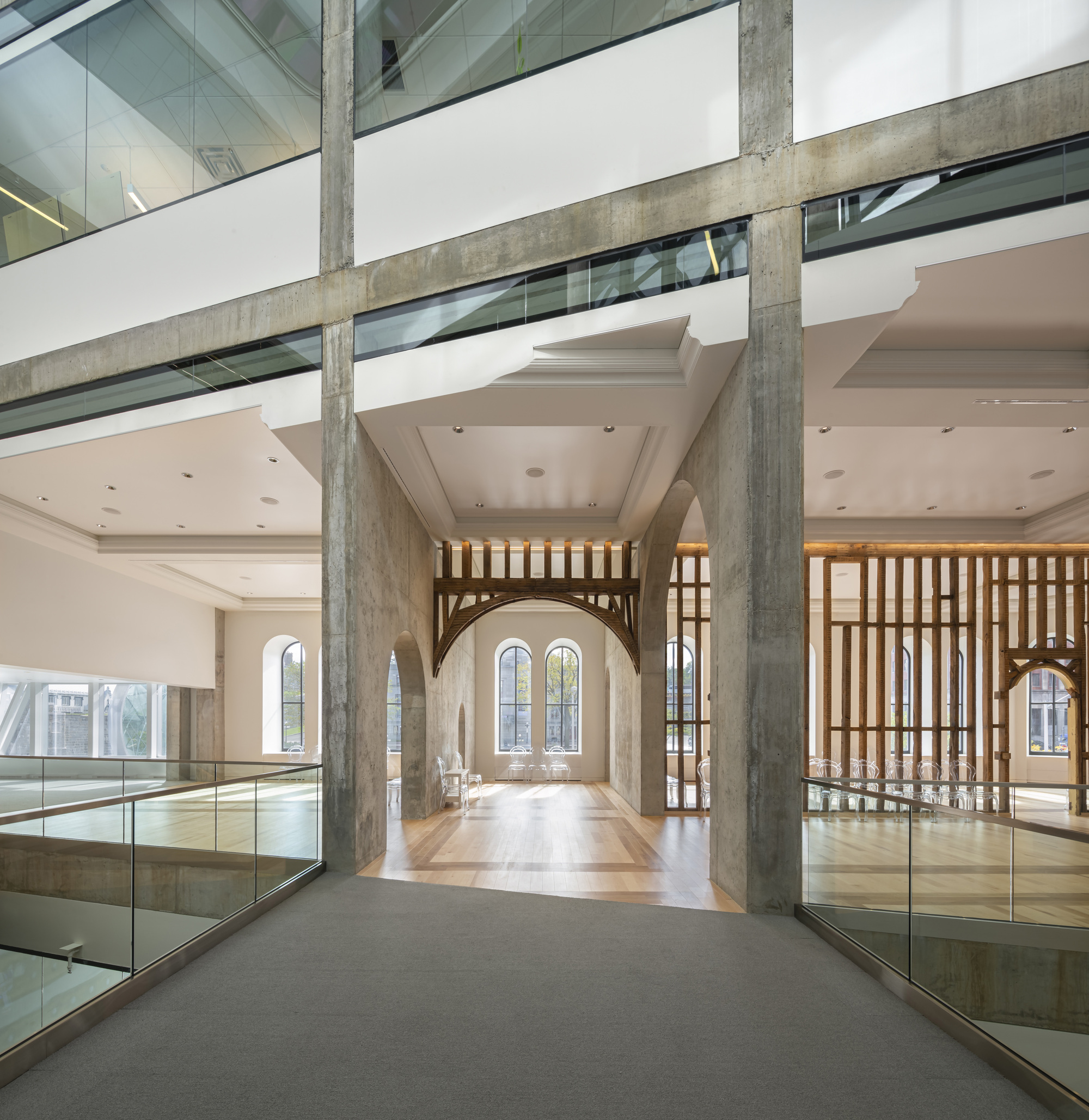 Interior bridge with exposed concrete columns spanning above a multi-level atrium space with glass balustrades