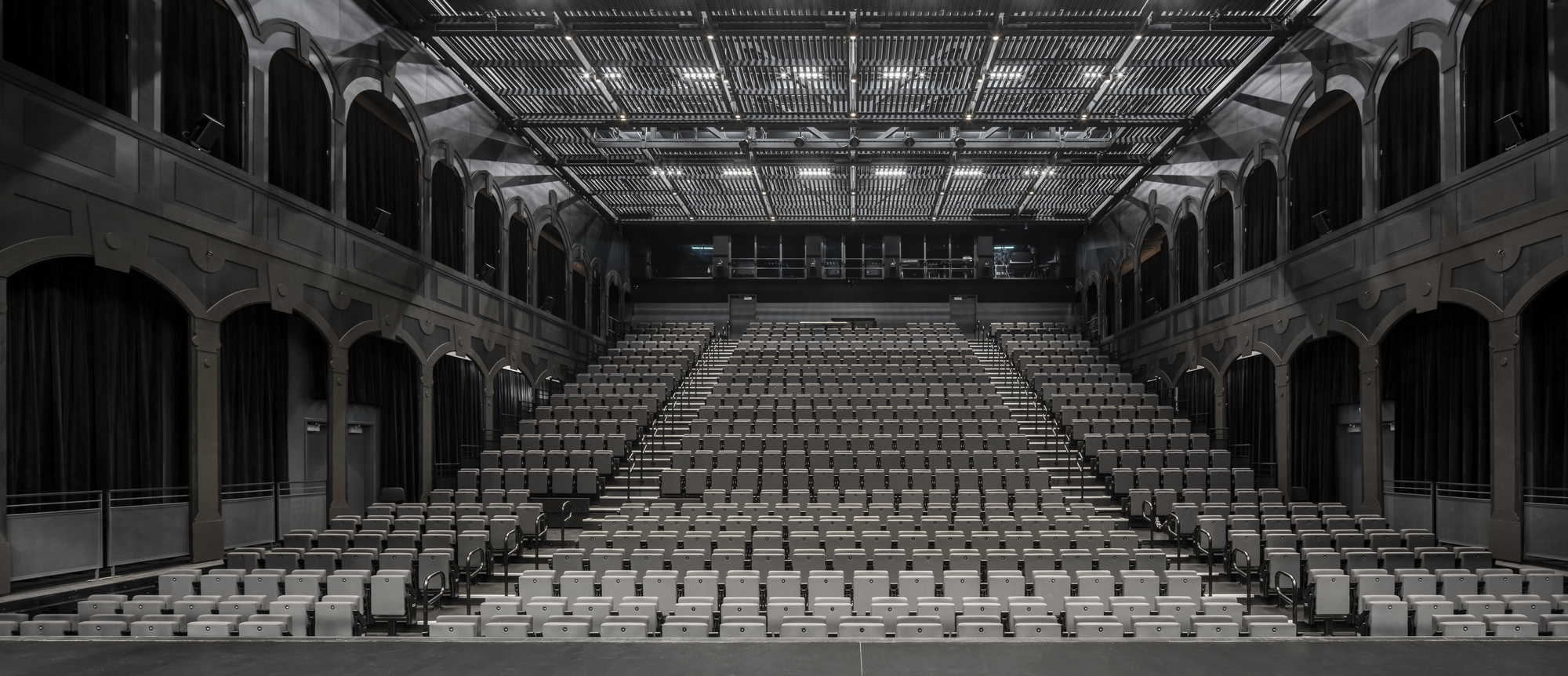 Interior view of the tiered seating hall with exposed mechanical ceiling and arched gallery openings