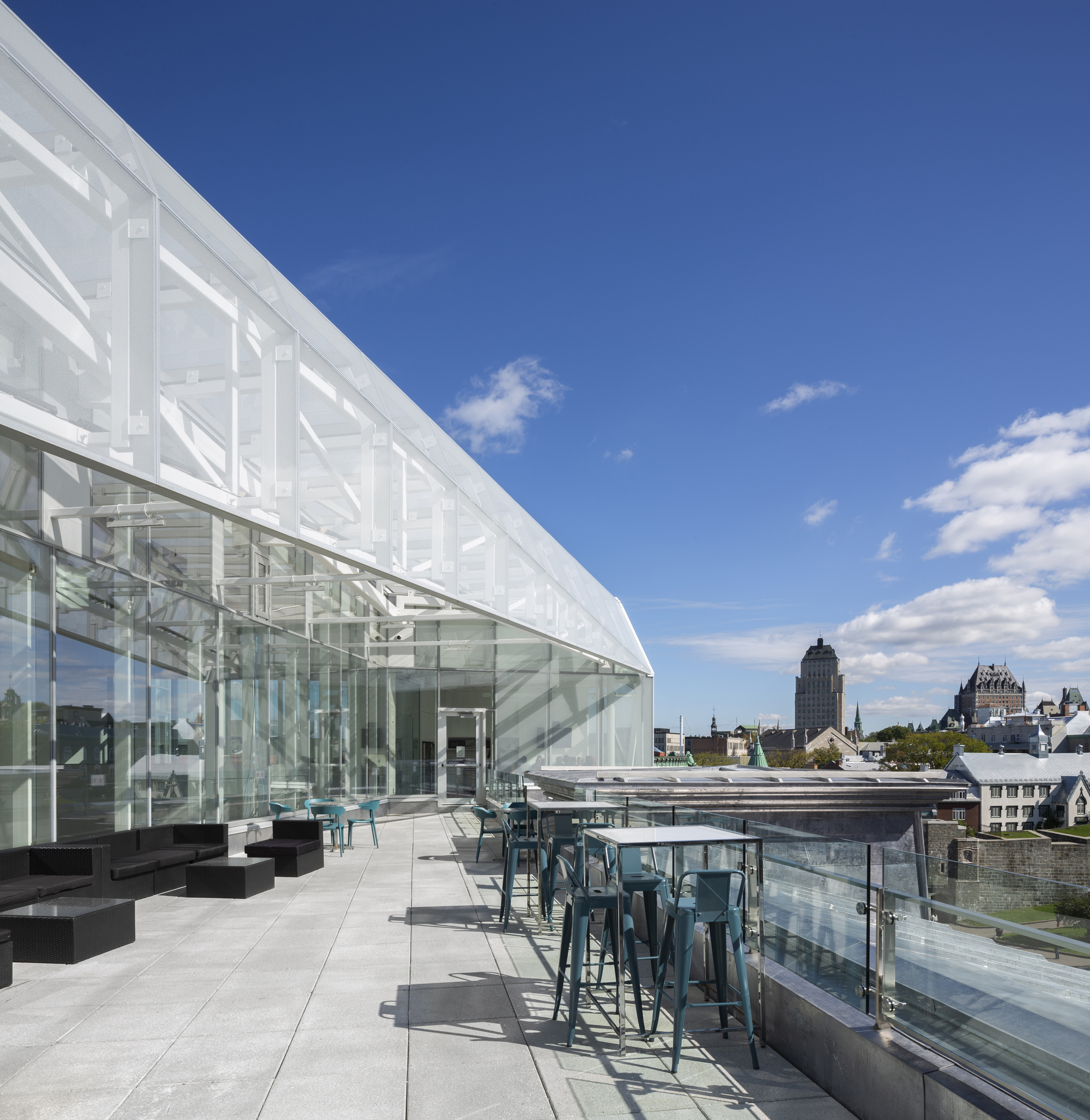 Rooftop terrace with glass pavilion, high tables and chairs overlooking the historic skyline under blue sky