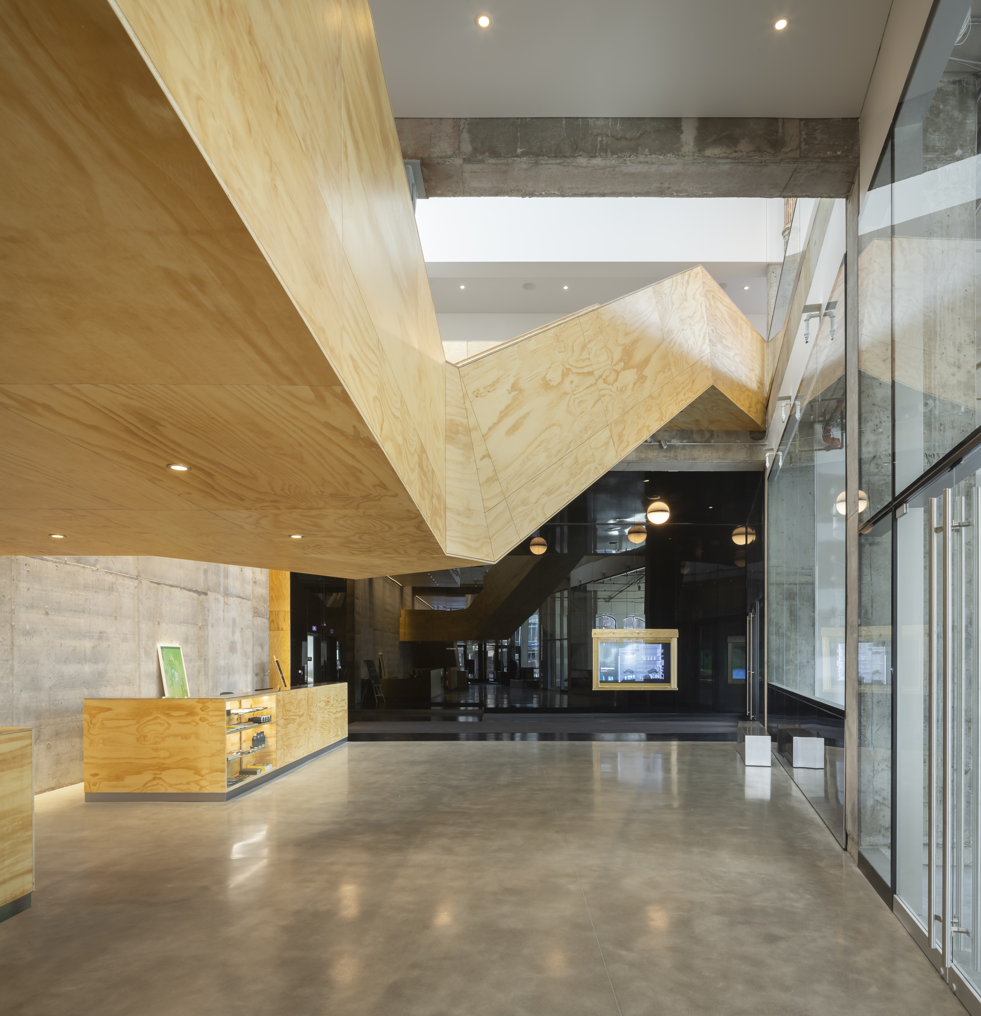 Interior view of folded plywood stair volume suspended between concrete walls and glass partitions