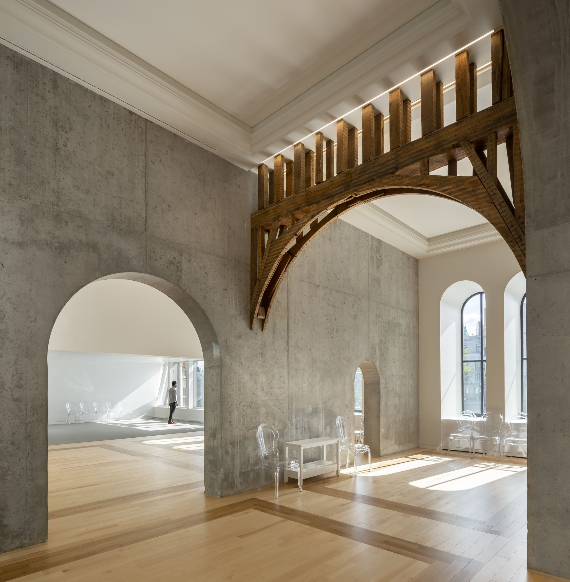Concrete wall with arched opening and timber truss support beneath a slatted wooden screen in bright sunlight