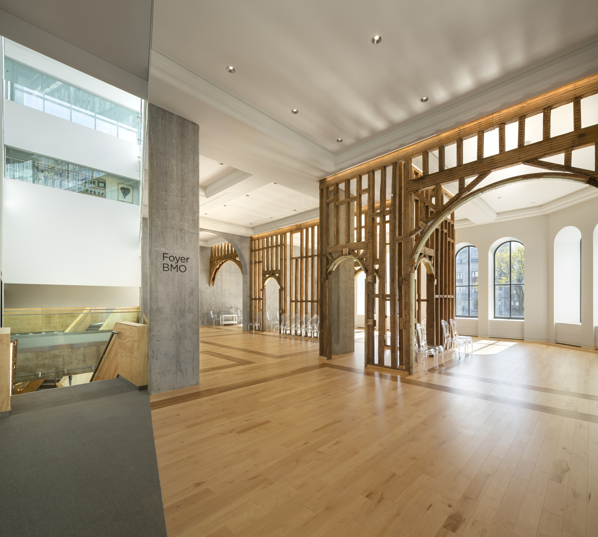 Open foyer with timber screen partitions framing concrete arches, oak flooring, and arched windows admitting afternoon light