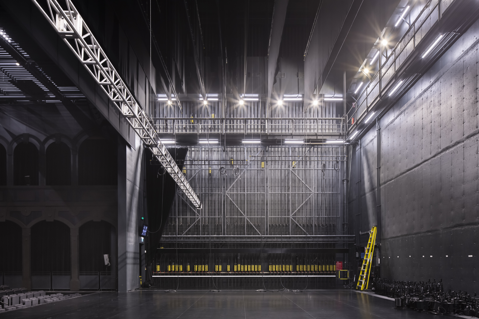Stage fly tower with diagonal steel bracing and catwalks under theatrical lighting and rigging systems