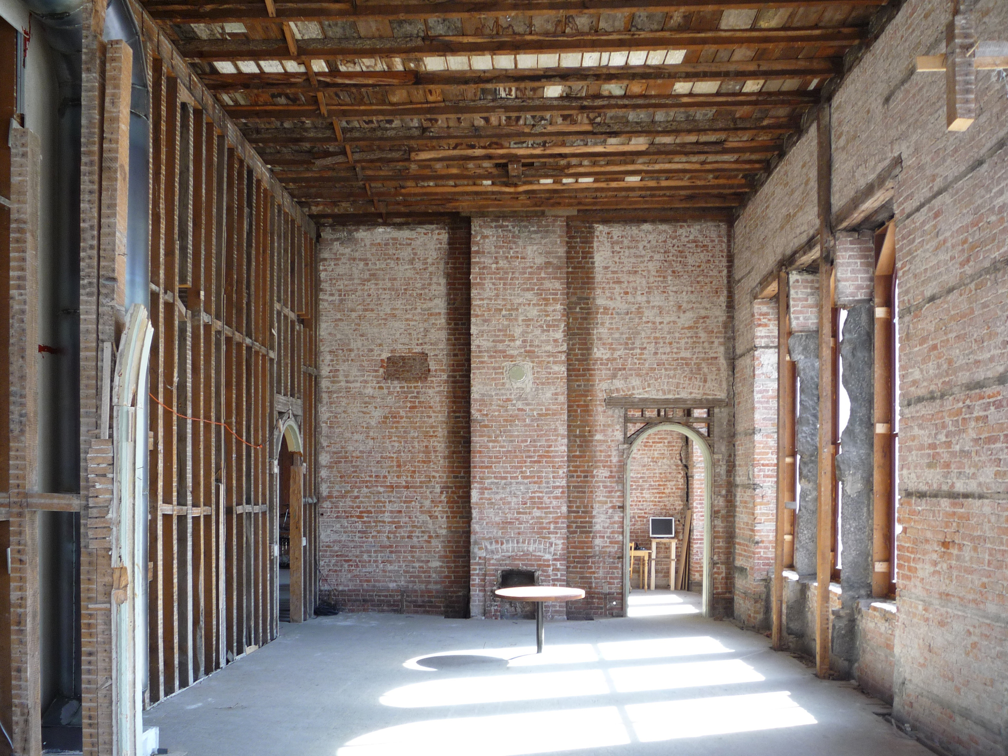 Exposed brick interior room with timber beamed ceiling and arched doorway allowing sunlight through