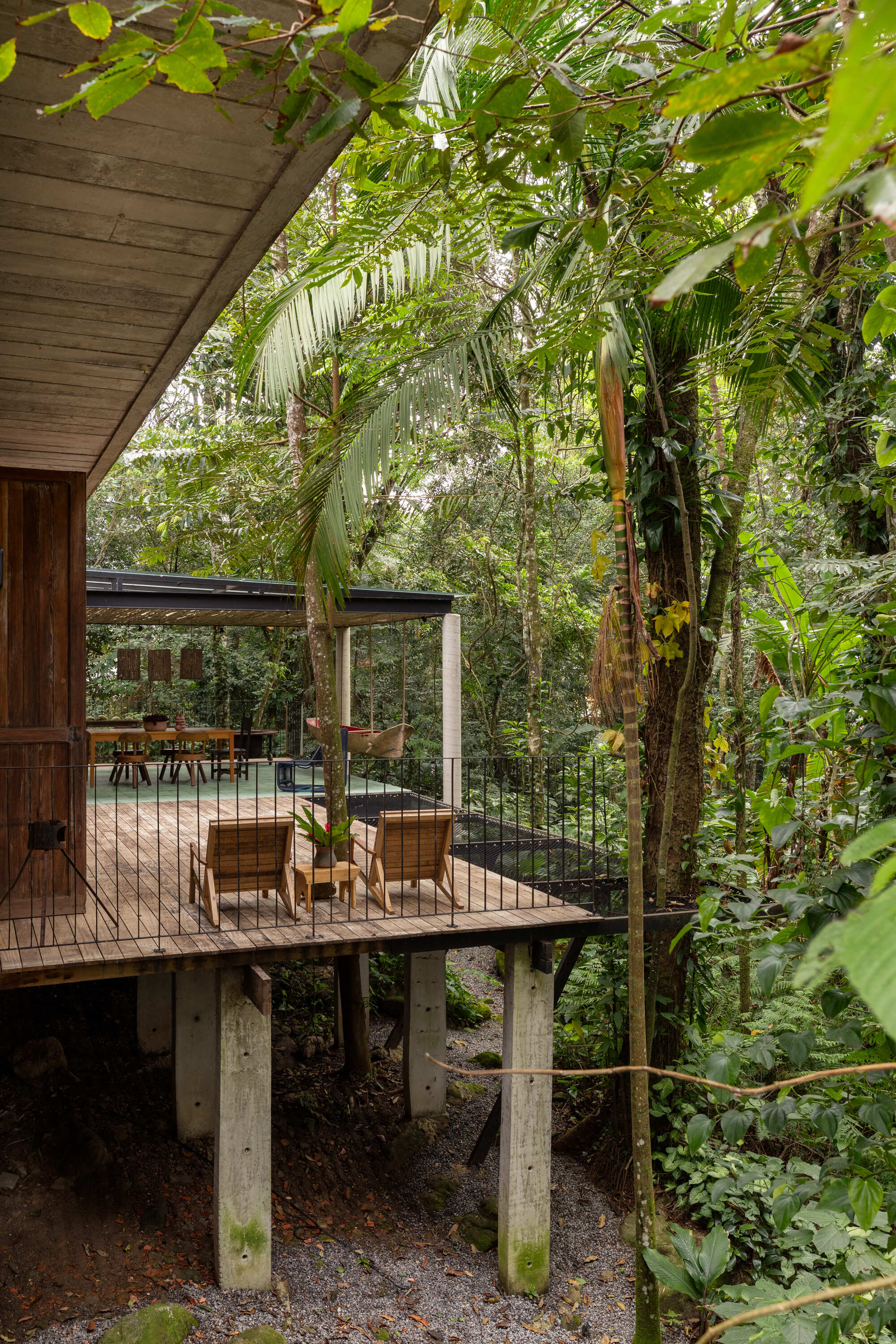 Elevated timber deck on concrete piers with wicker chairs beneath overhanging palm fronds