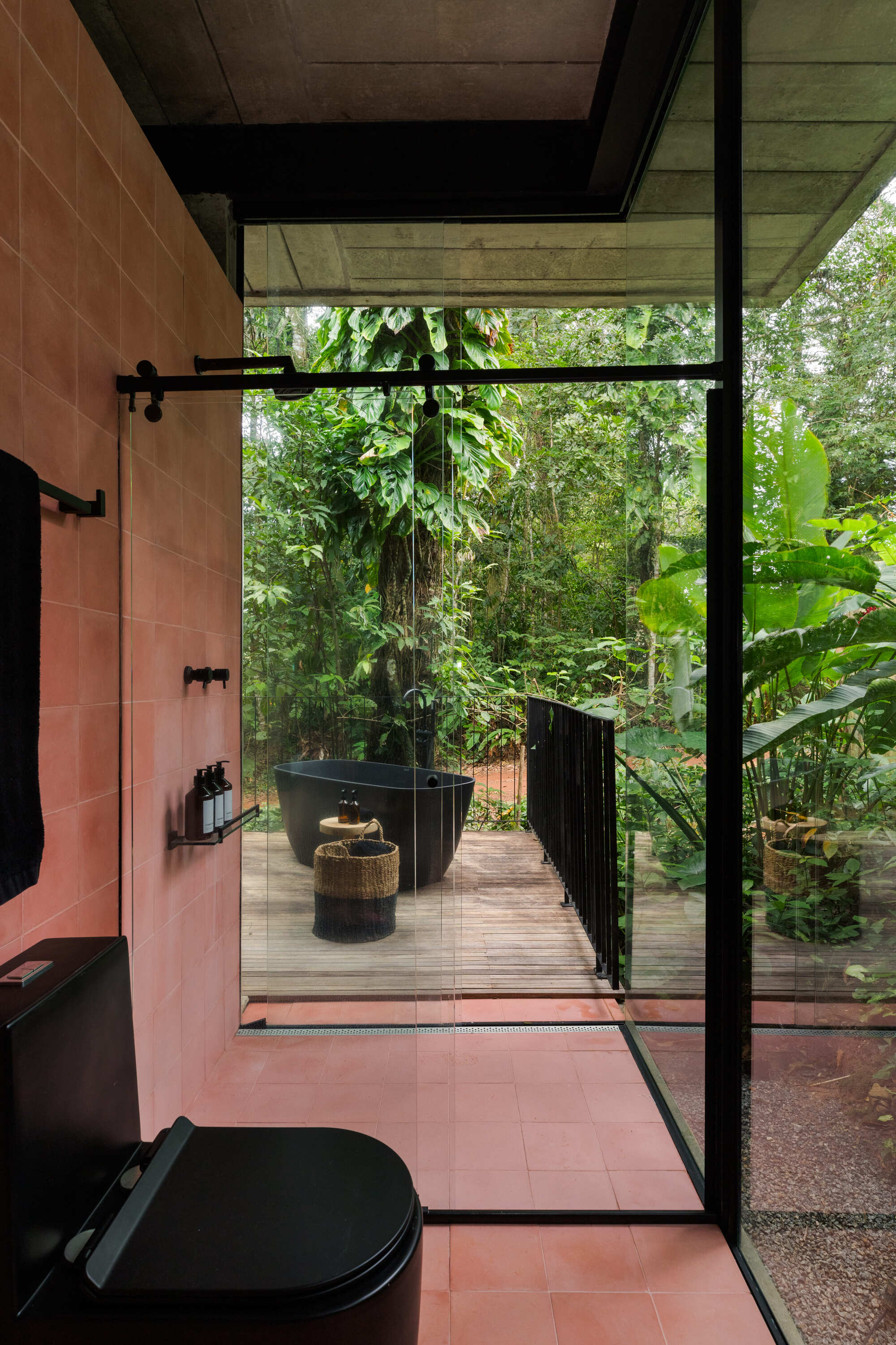 Bathroom with terracotta tile floor and walls leading to timber deck terrace surrounded by jungle canopy