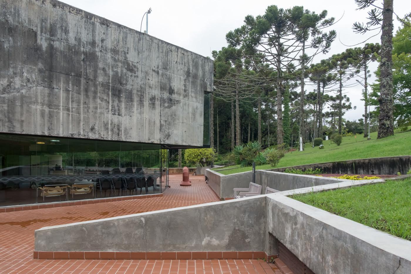 Terraced courtyard with concrete retaining walls and red brick paving beneath a cantilevered volume and pines