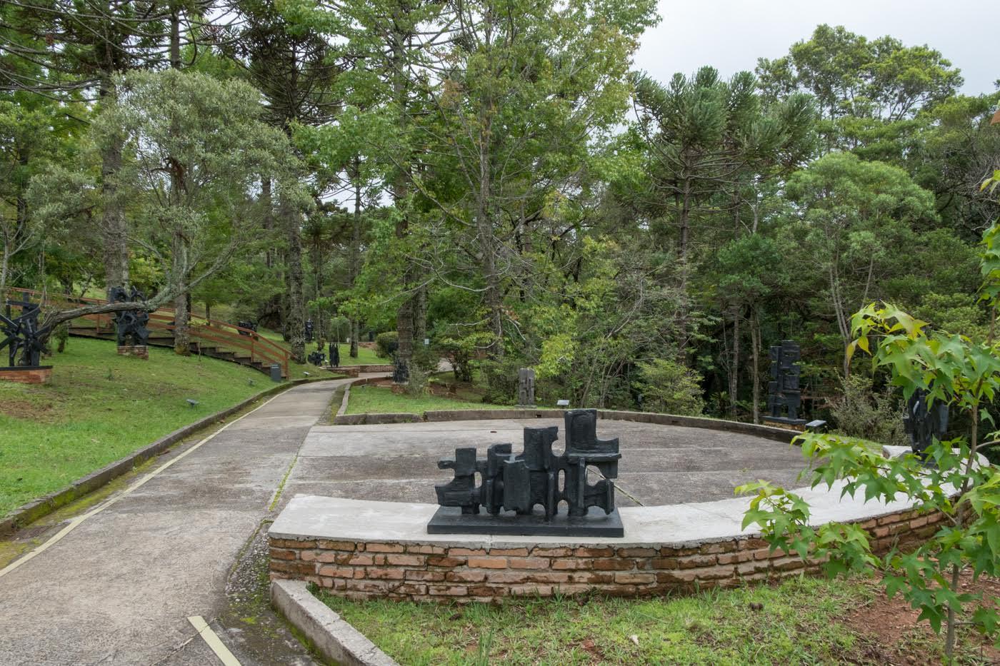 Circular concrete platform with black steel sculpture set within a sloped landscape of trees and grass