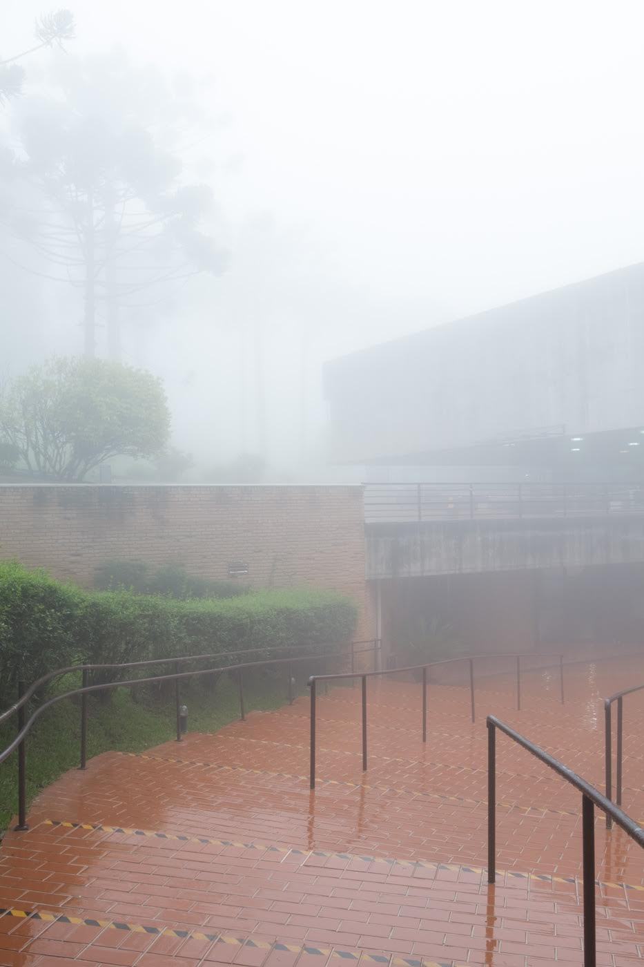 Brick staircase with metal railings descending through dense fog toward a courtyard and concrete walls