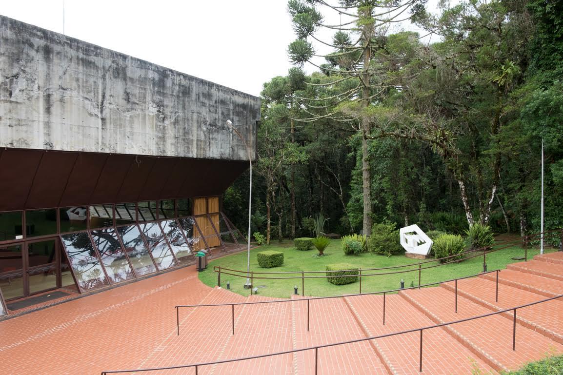 Cantilevered concrete volume above a glazed facade overlooking stepped brick terraces and a lawn with sculptures