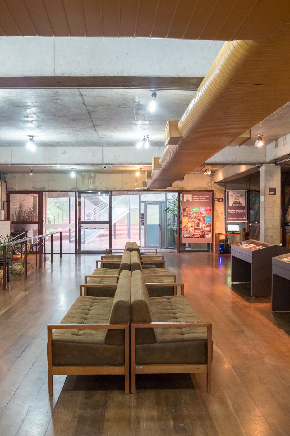 Interior lobby with exposed concrete ceiling, wood paneling, and green upholstered seating along polished floors
