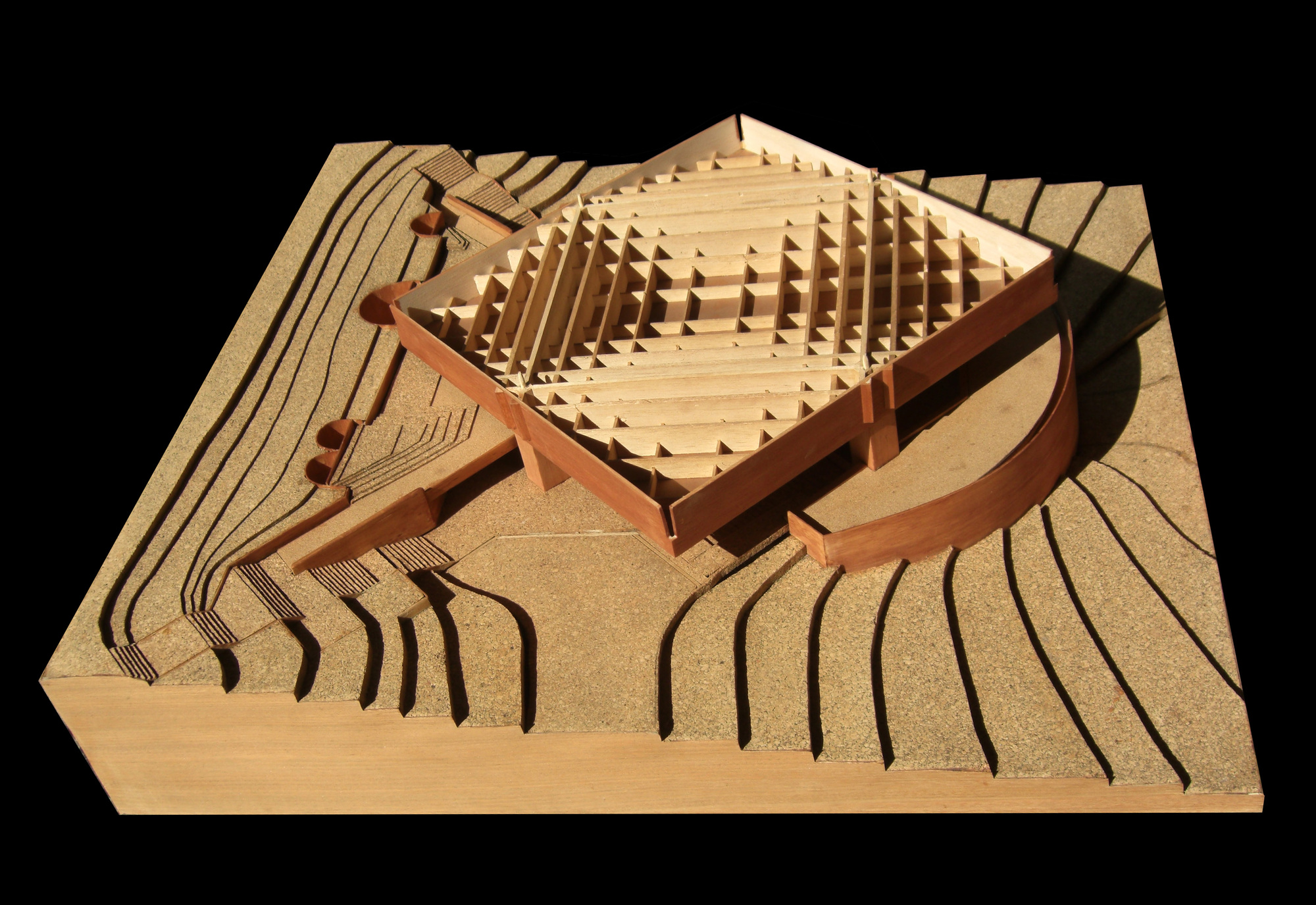 Physical model showing terraced landscape with timber-framed pavilion and curving wall under directional lighting