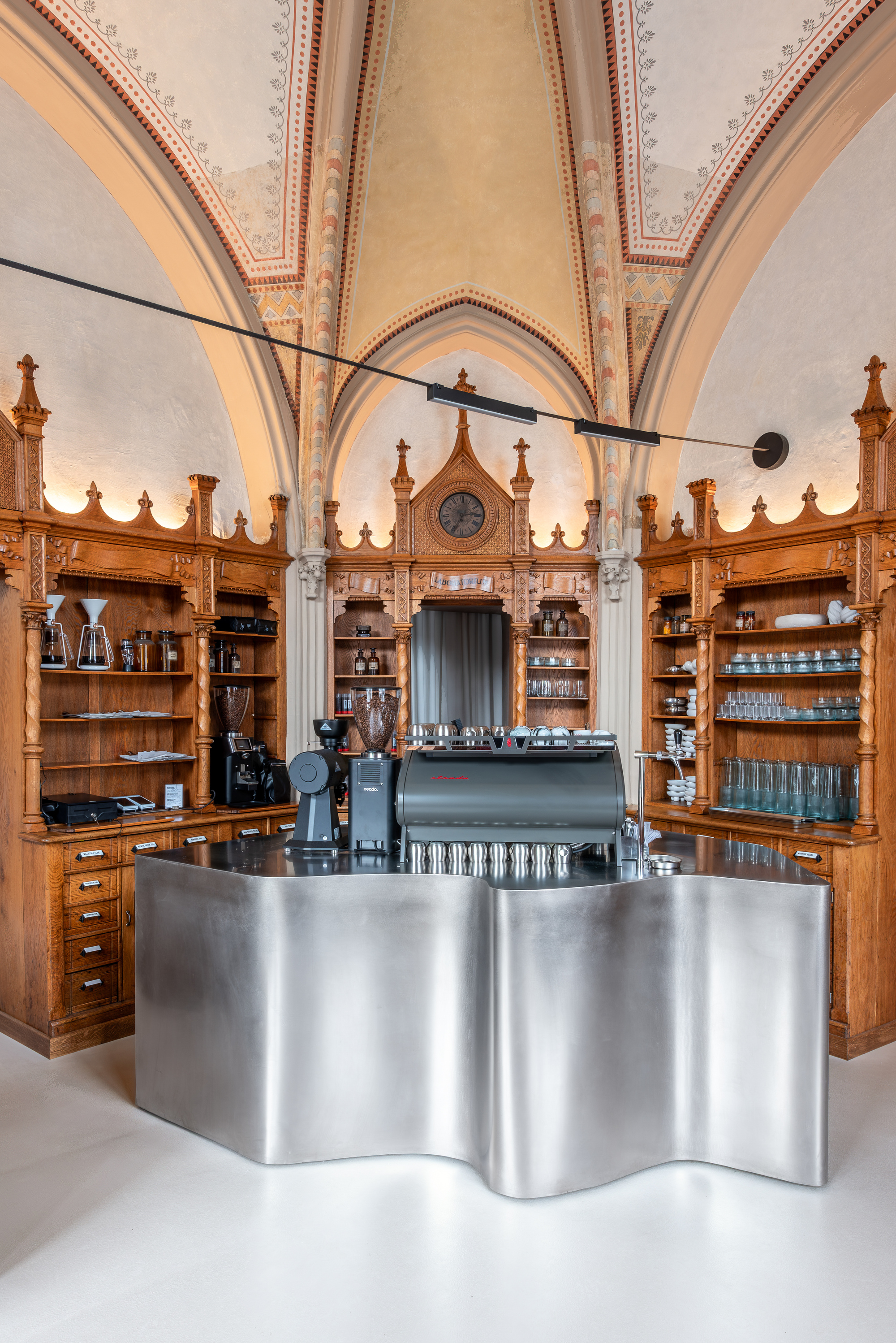 Curved metal coffee bar countertop with espresso machine against ornate oak millwork and shelving
