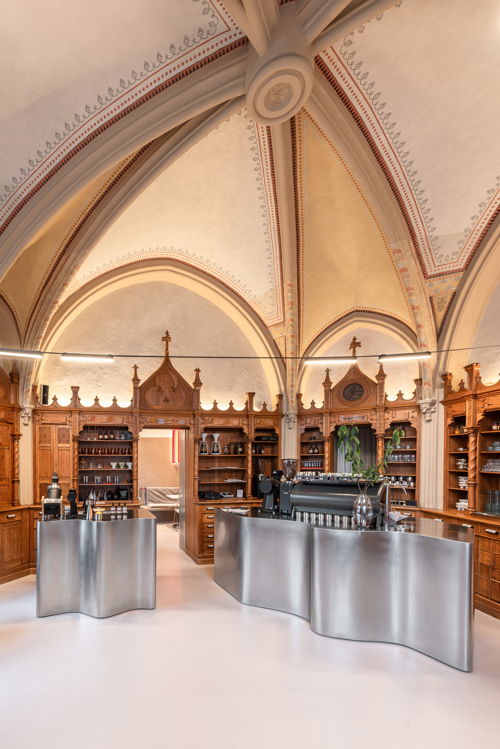 Two freestanding steel service counters in vaulted space with decorative plasterwork and timber display shelves