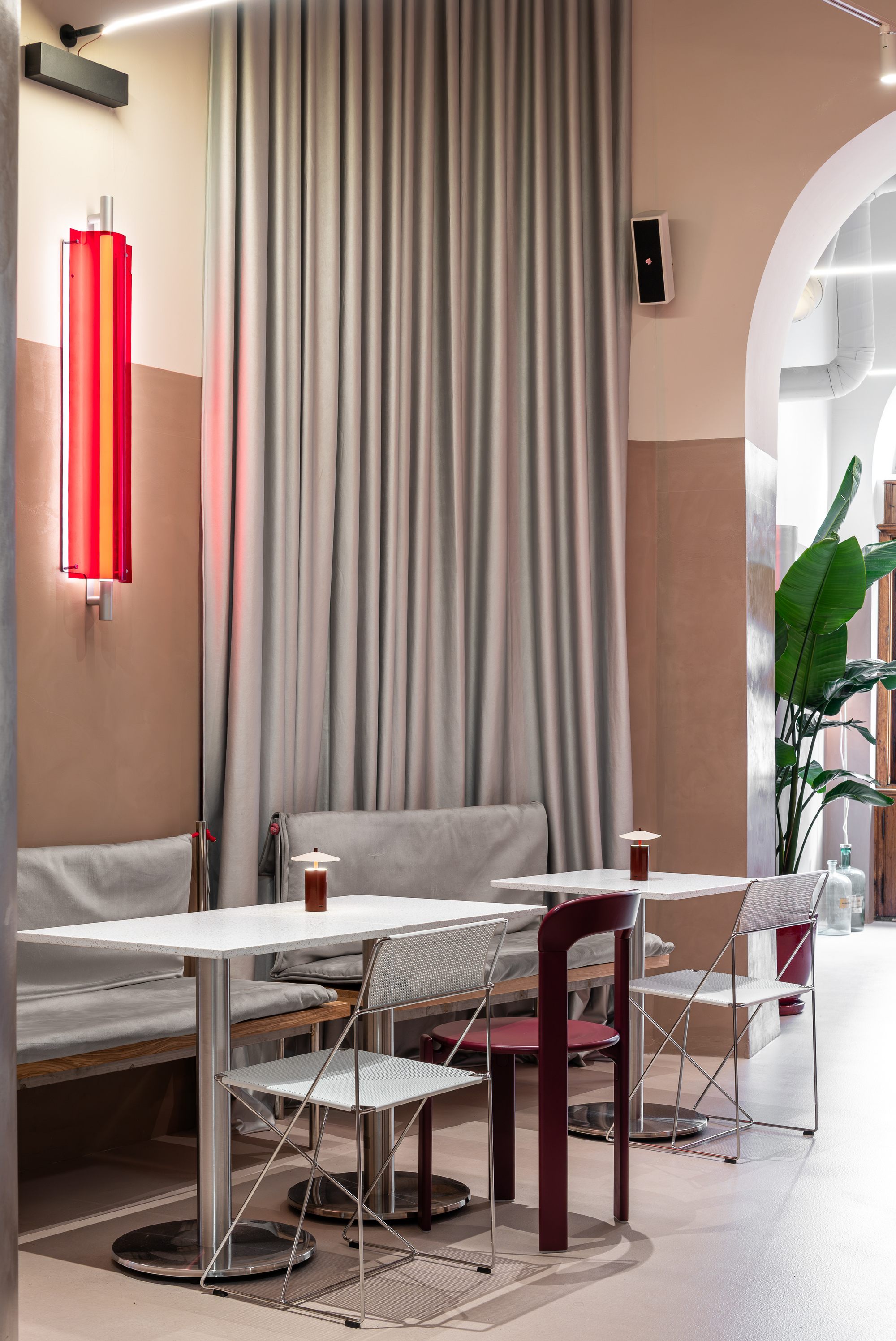 Seating area with white tables and mixed chairs below floor-to-ceiling curtain and vertical tube light