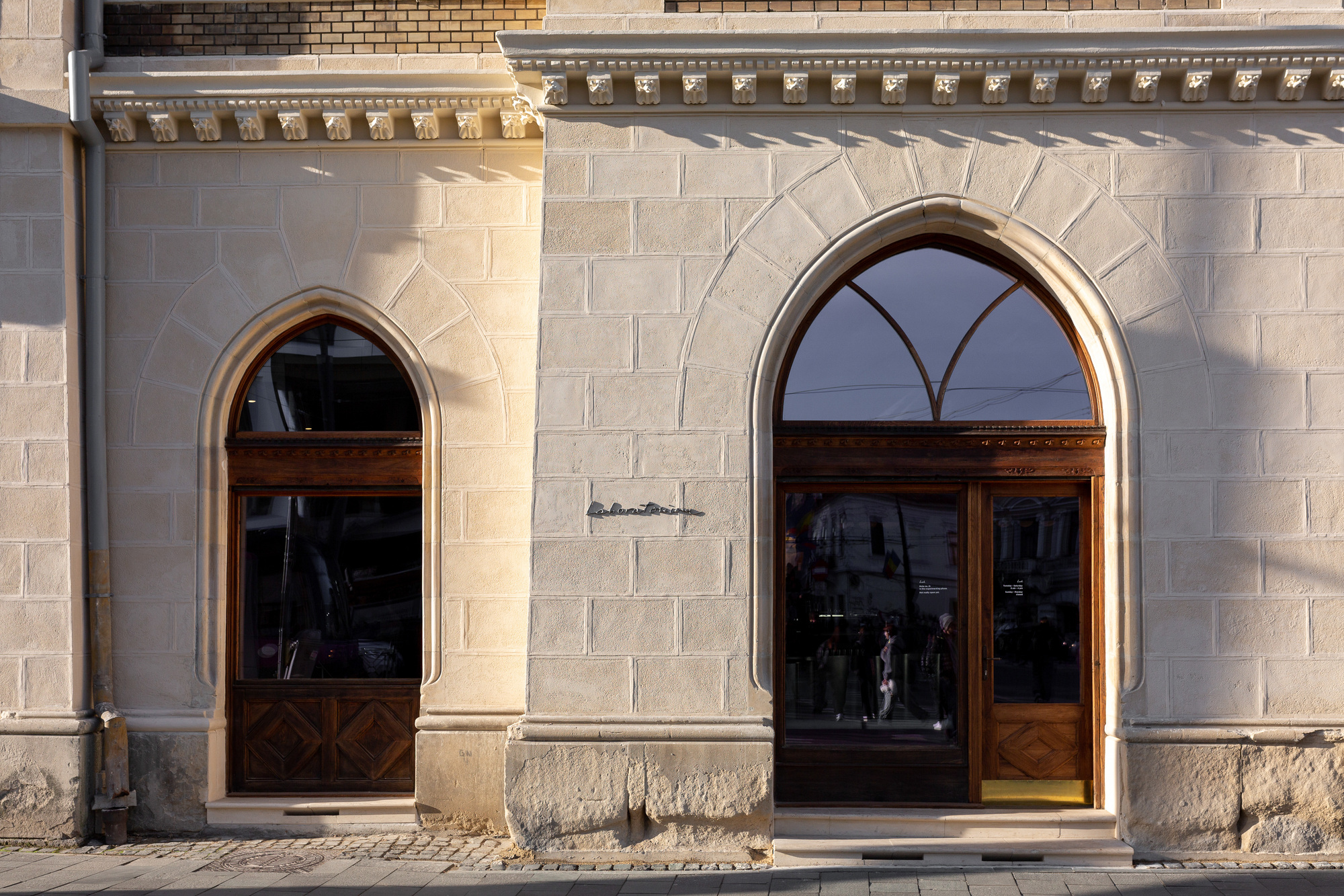 Two arched doorways with dark timber frames set in a pale stone facade in morning light