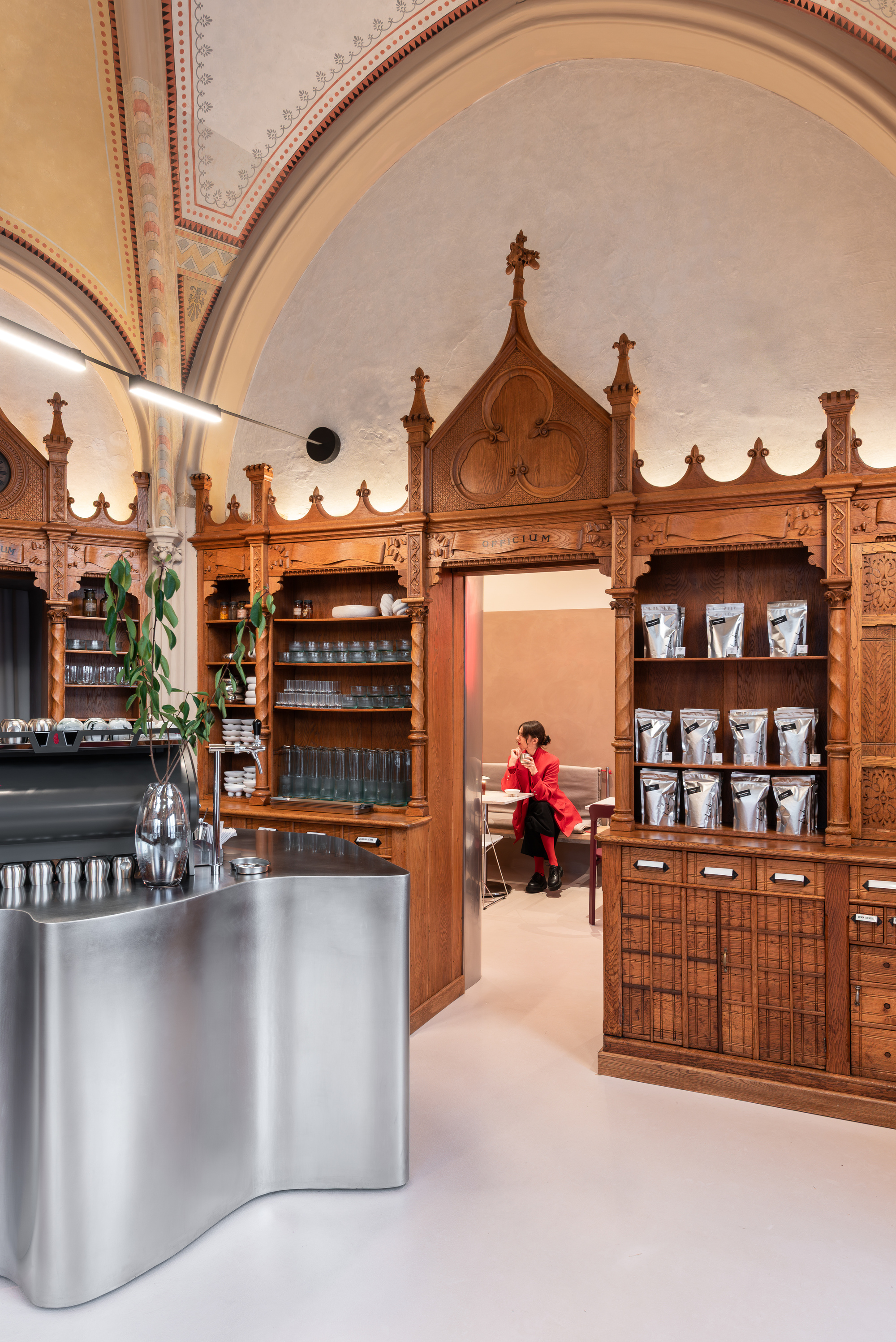 Carved timber shelving with Gothic pinnacles above a stainless steel counter with person seated in background