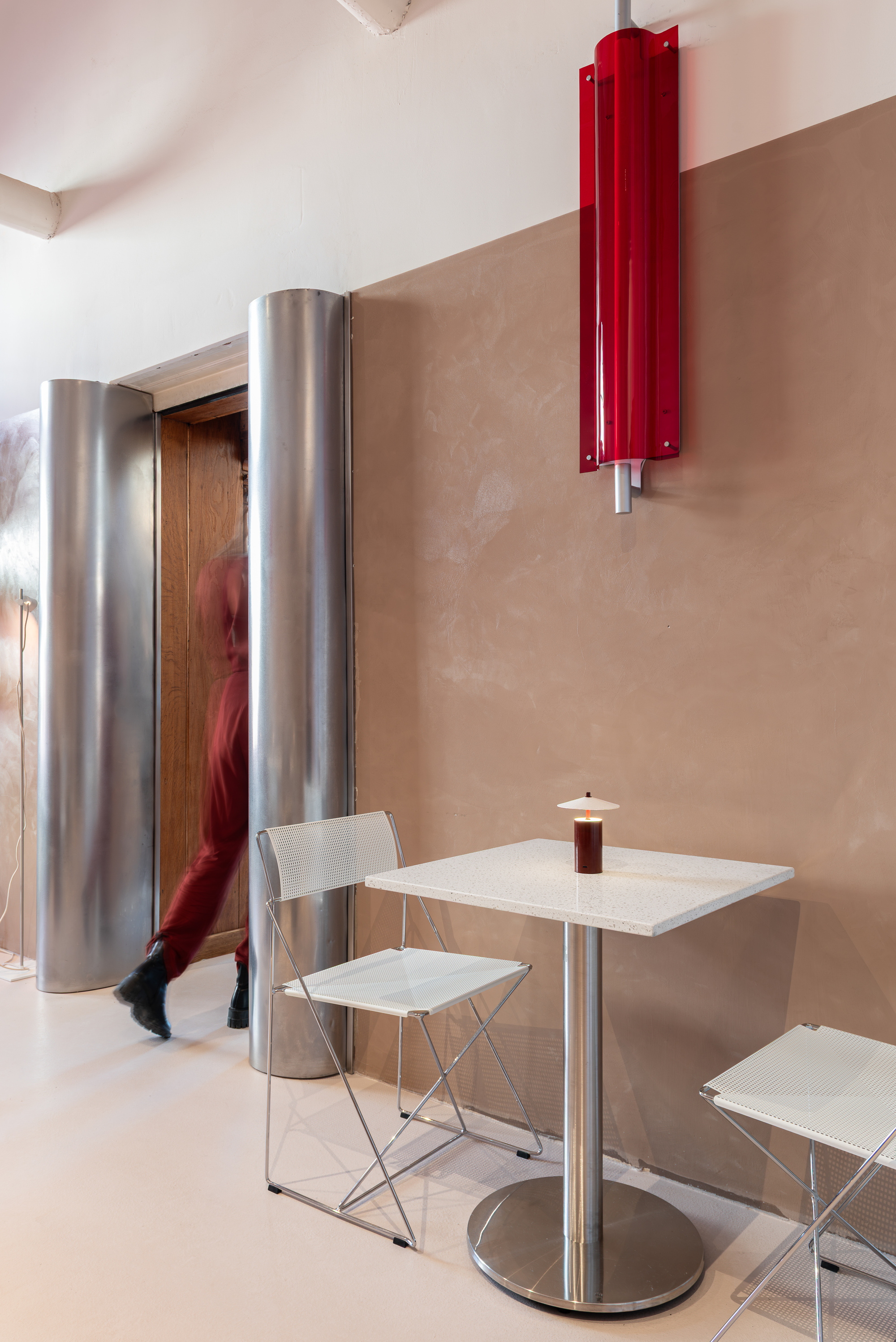 Interior seating area with cylindrical steel columns, a red wall-mounted radiator, and a person walking past