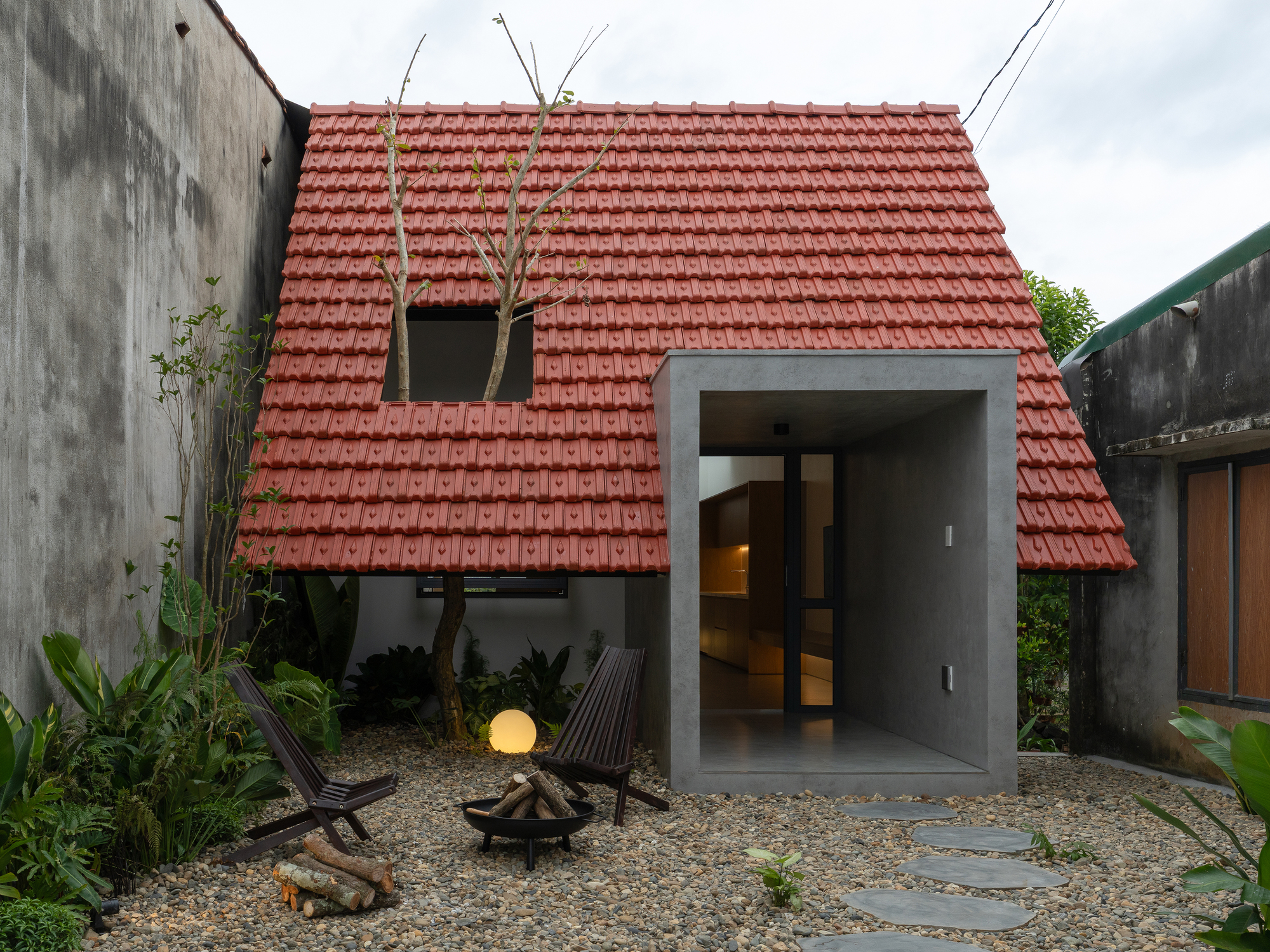 Gabled red tile roof rising above a concrete framed entrance and gravel courtyard at dusk